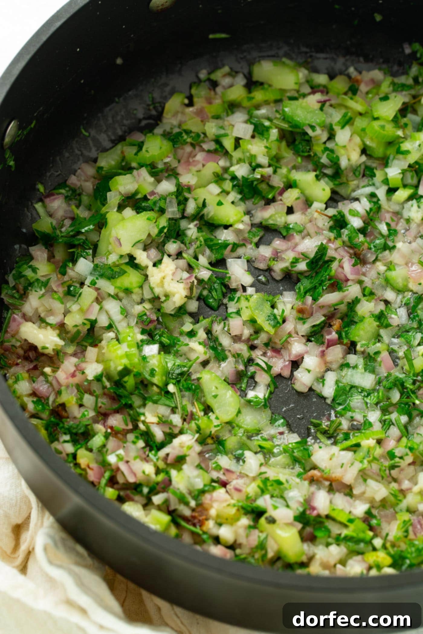 A photo of beautifully sauteed shallots, celery, garlic and fresh herbs in a skillet, showcasing the aromatic foundation of the stuffing.