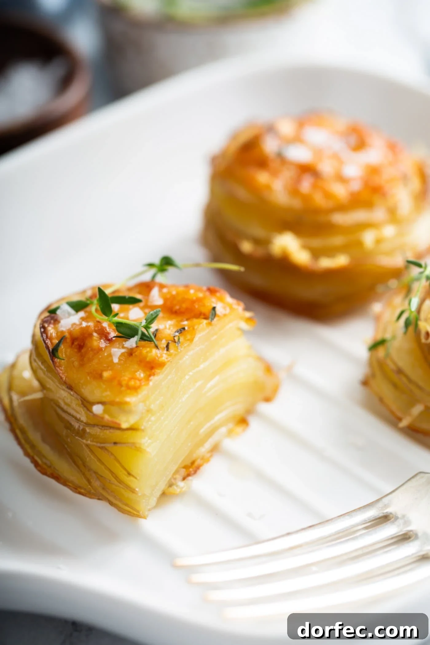 Gruyere potatoes on parchment paper. One stack of potatoes has been cut in half. They are baked to a golden brown.