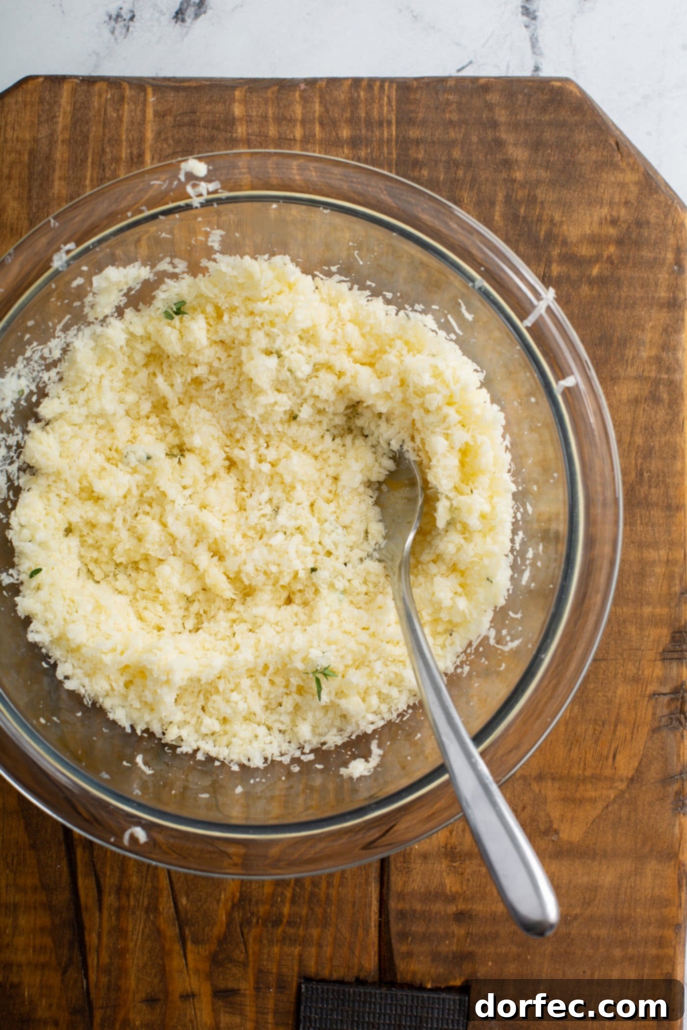 A bowl with shredded cheeses, garlic, salt and pepper. There is a spoon in the bowl.
