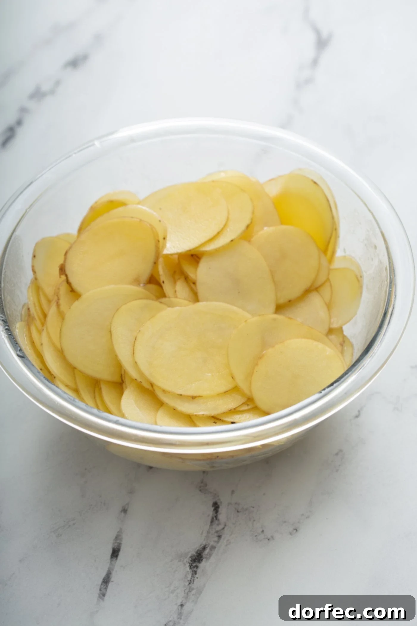 A clear glass bowl filled with sliced potatoes.