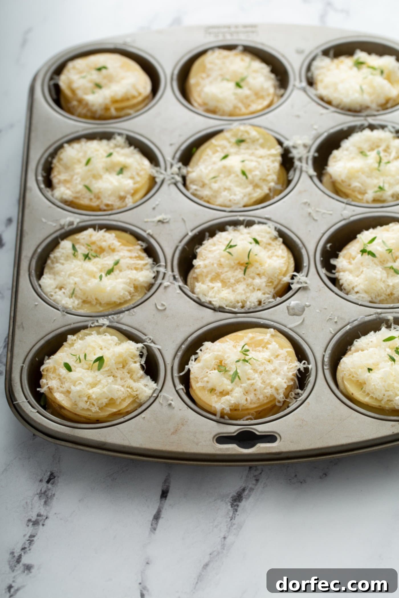 A muffin tin filled with sliced potatoes topped with shredded gruyer and parmesan cheeses.