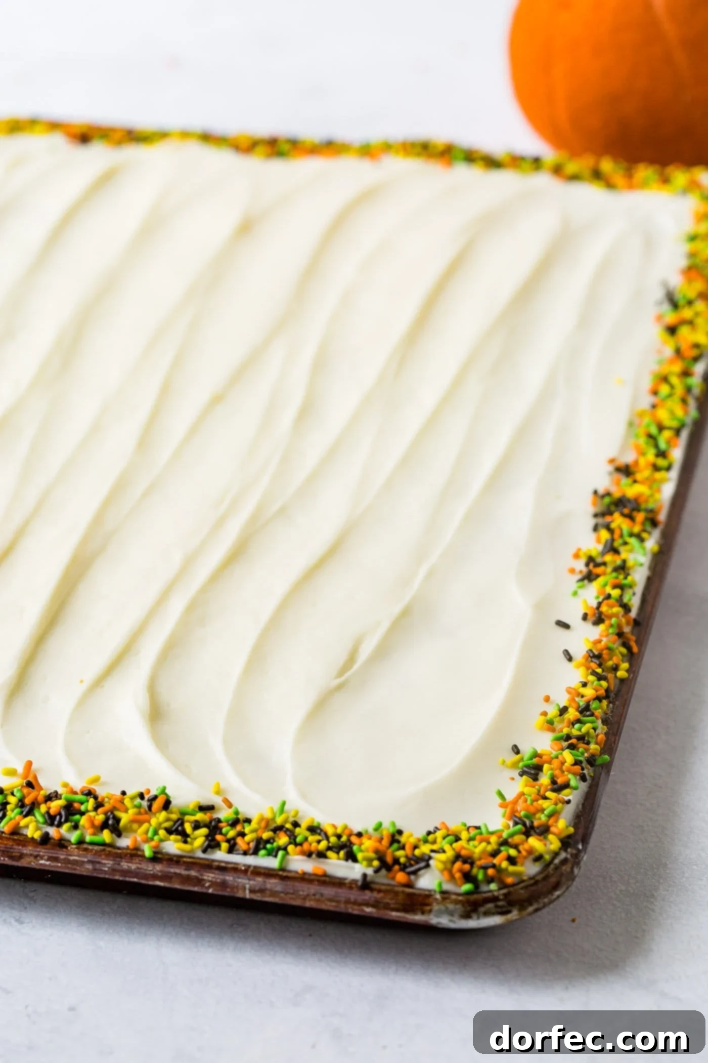 A photo of a whole pumpkin sheet cake that is frosted with cream cheese frosting and lined around the edges with fall sprinkles.