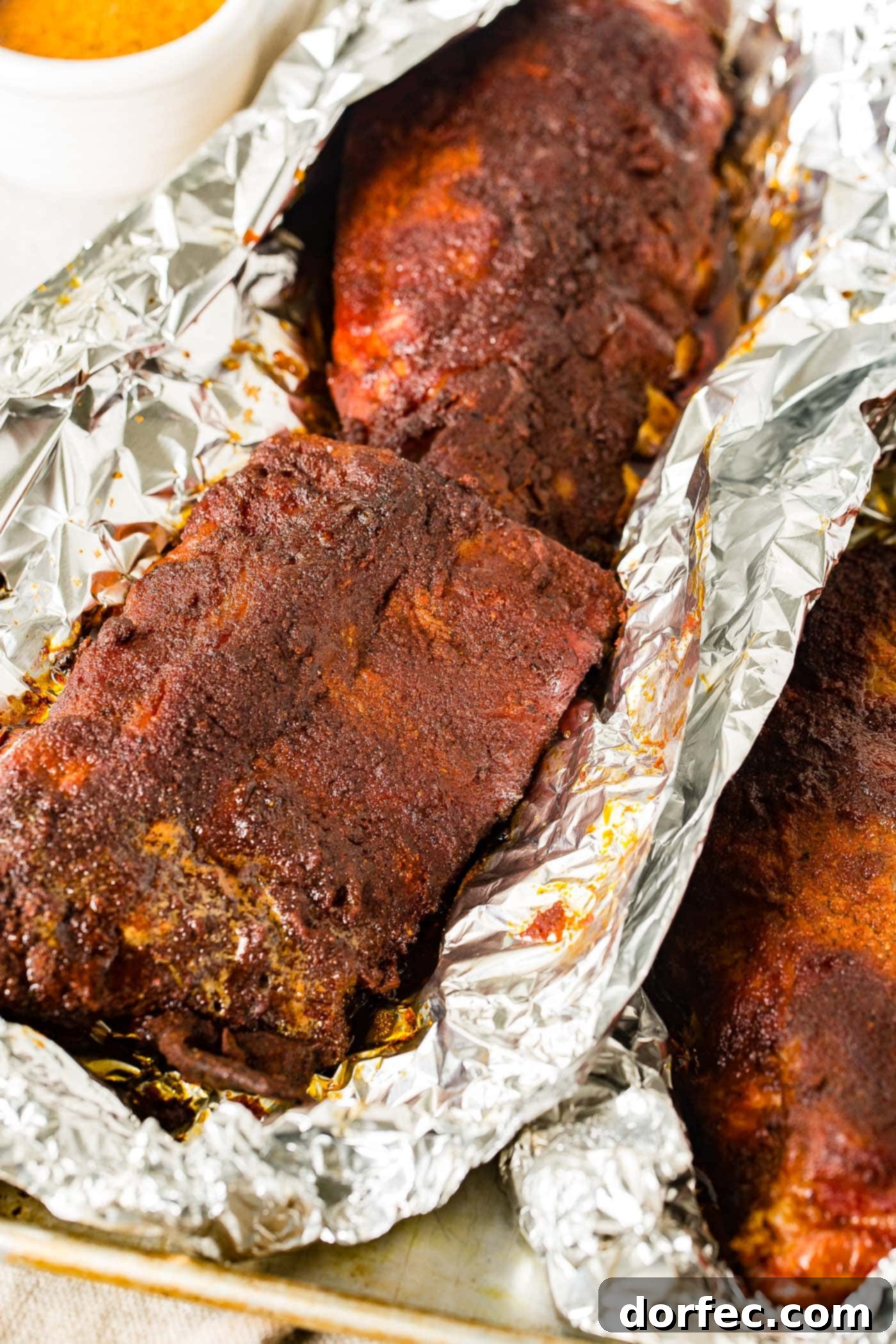 Traeger Smoked Ribs A rack of freshly smoked ribs, still wrapped in foil, with the top of the foil gently opened to reveal the succulent meat.