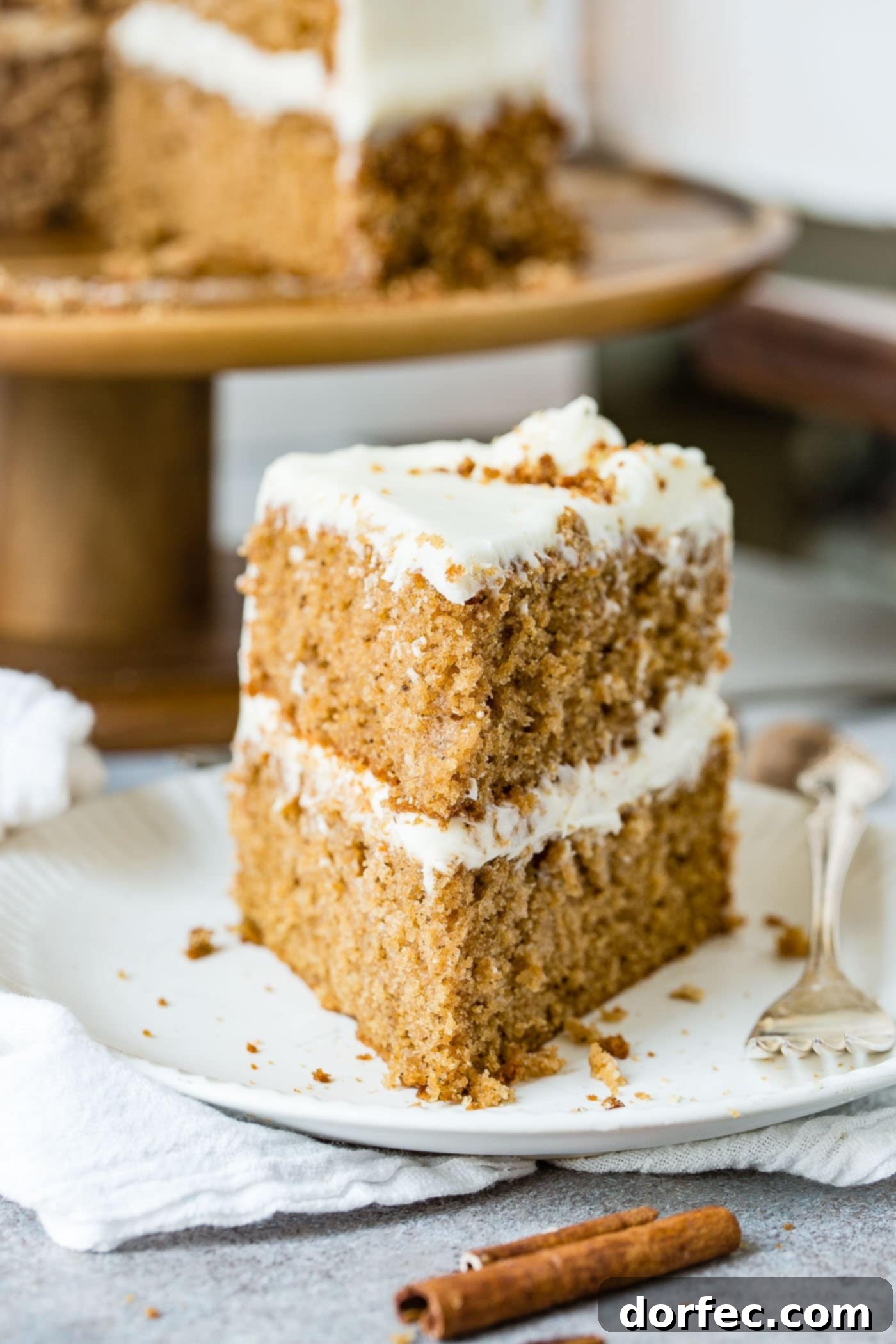 Delicious Slice of Spice Cake A generous slice of two-layer spice cake with cream cheese frosting, served on a white plate with a fork.