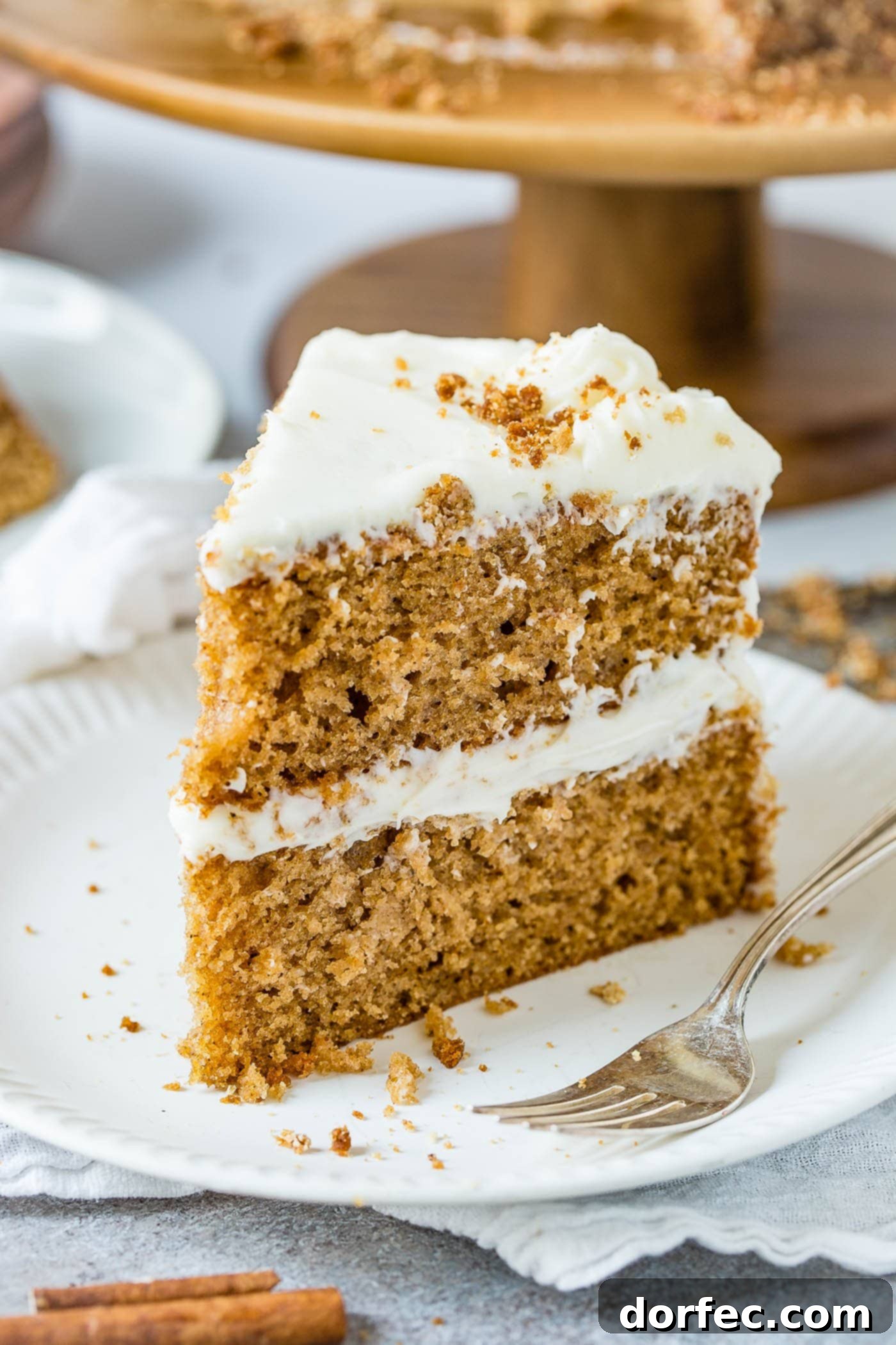 Inviting Slice of Spice Cake A mouth-watering slice of two-layer spice cake with fluffy cream cheese frosting, presented on a white dessert plate with a silver fork.