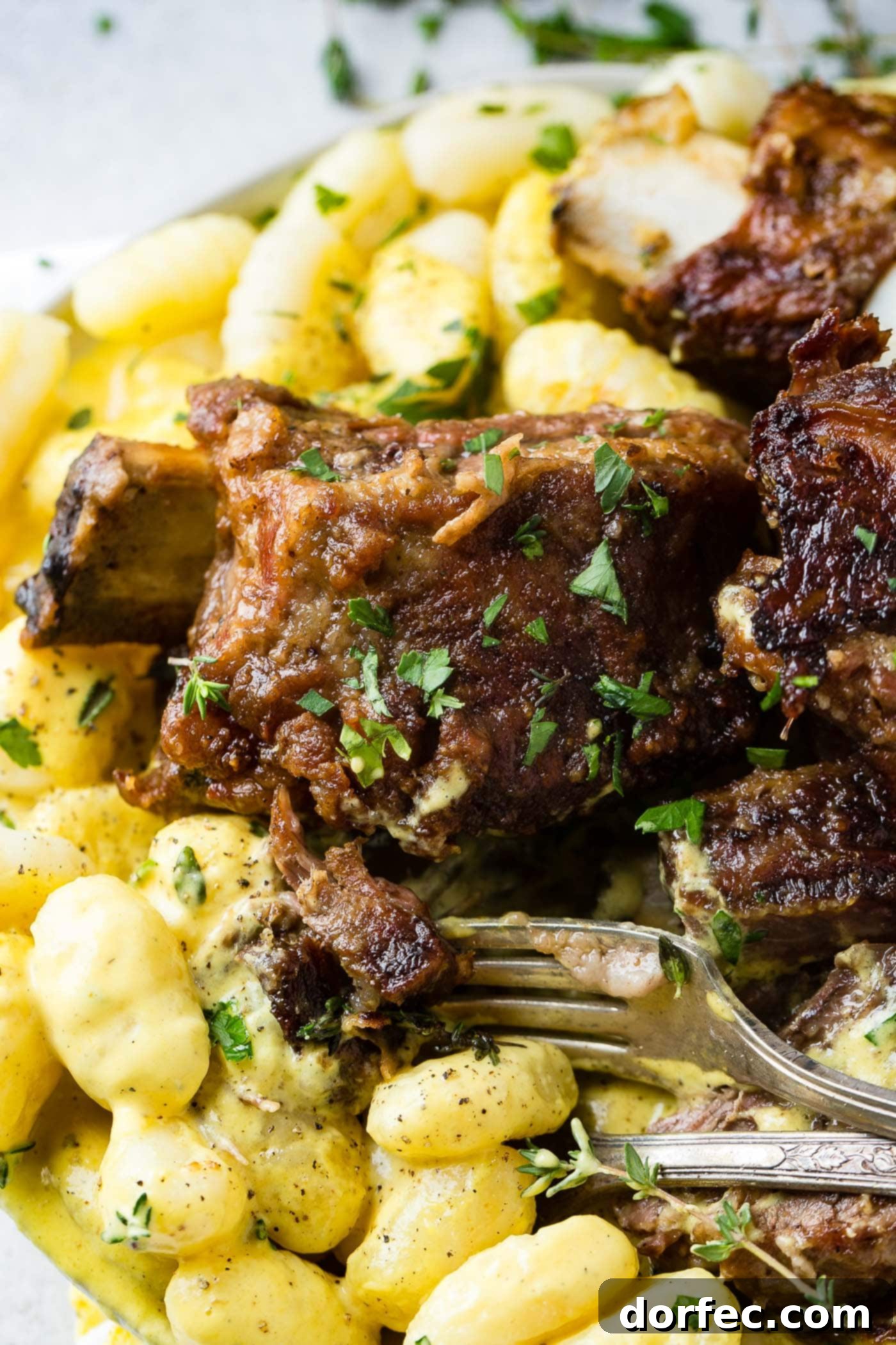 A close-up of a fork lifting a bite of succulent braised beef short rib and creamy charred pepper gnocchi from a plate, showcasing the dish's rich texture.