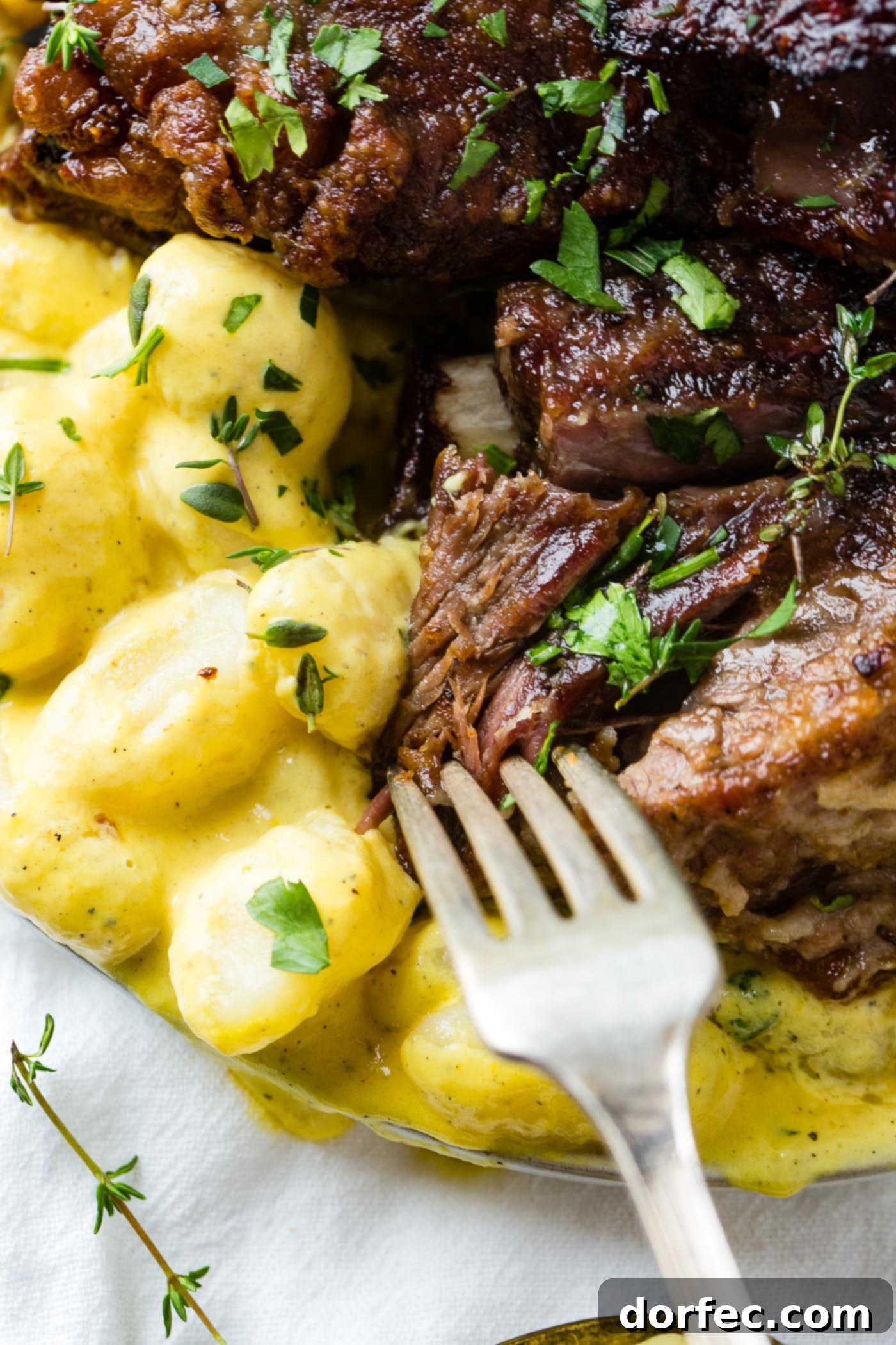 A close-up shot of a fork scooping up a portion of tender braised beef short ribs and creamy charred pepper gnocchi from a plate, highlighting the enticing sauce and textures.