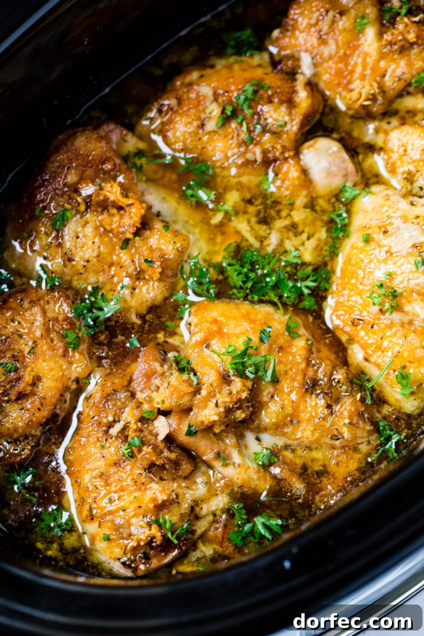 A photo of slow cooker chicken in a crock pot, garnished with fresh herbs, ready to be served.