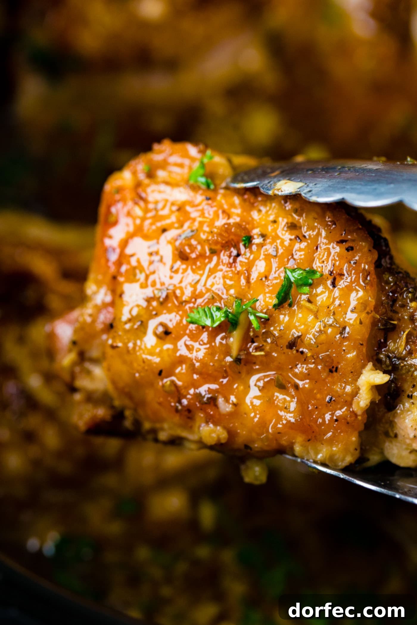 A photo of one perfectly cooked chicken thigh being held up by metal tongs from our slow cooker garlic chicken recipe, showcasing its crispy skin and juicy interior.