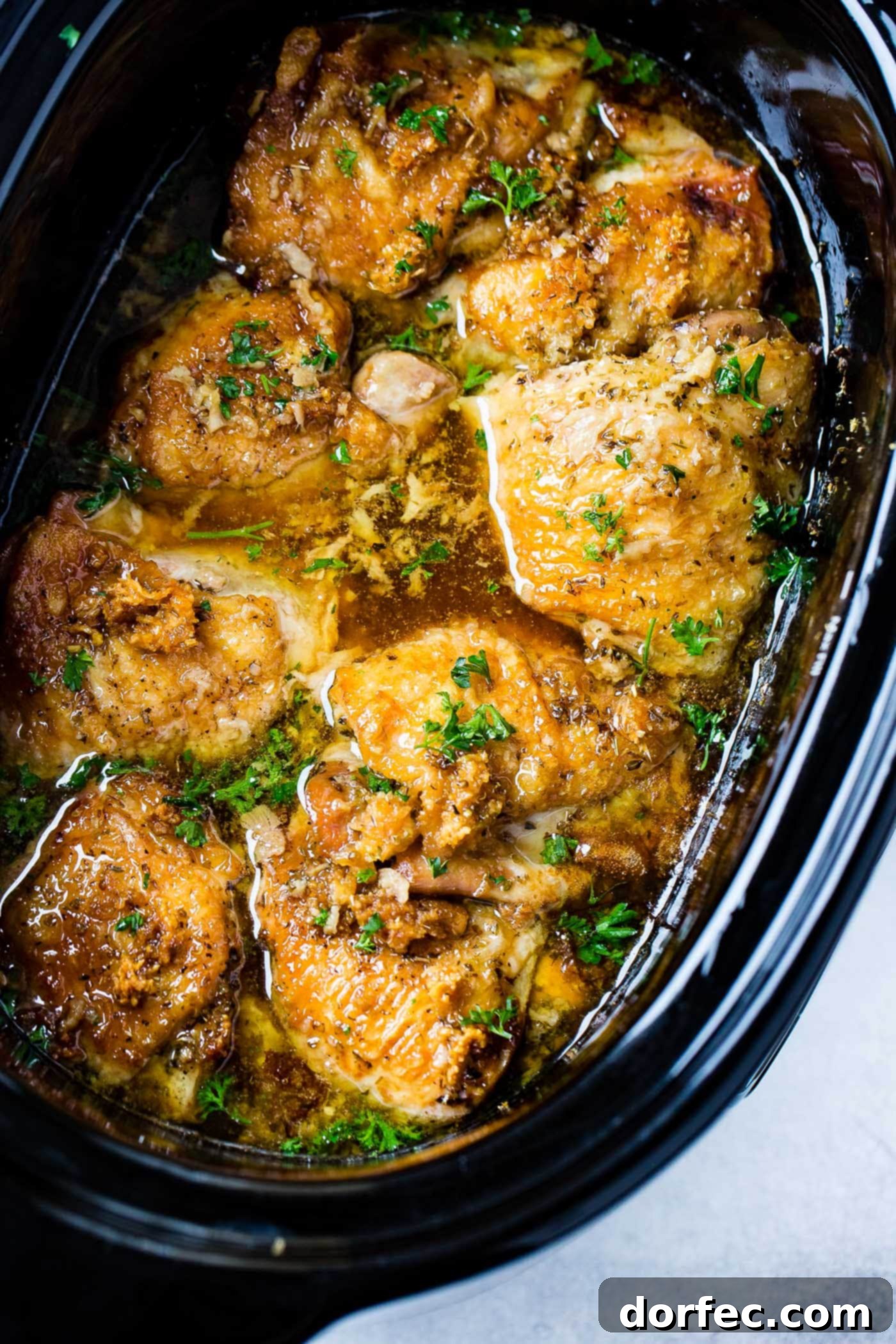 A photo of slow cooker chicken in a crock pot topped with fresh chopped parsley, steam rising, indicating it's hot and ready.