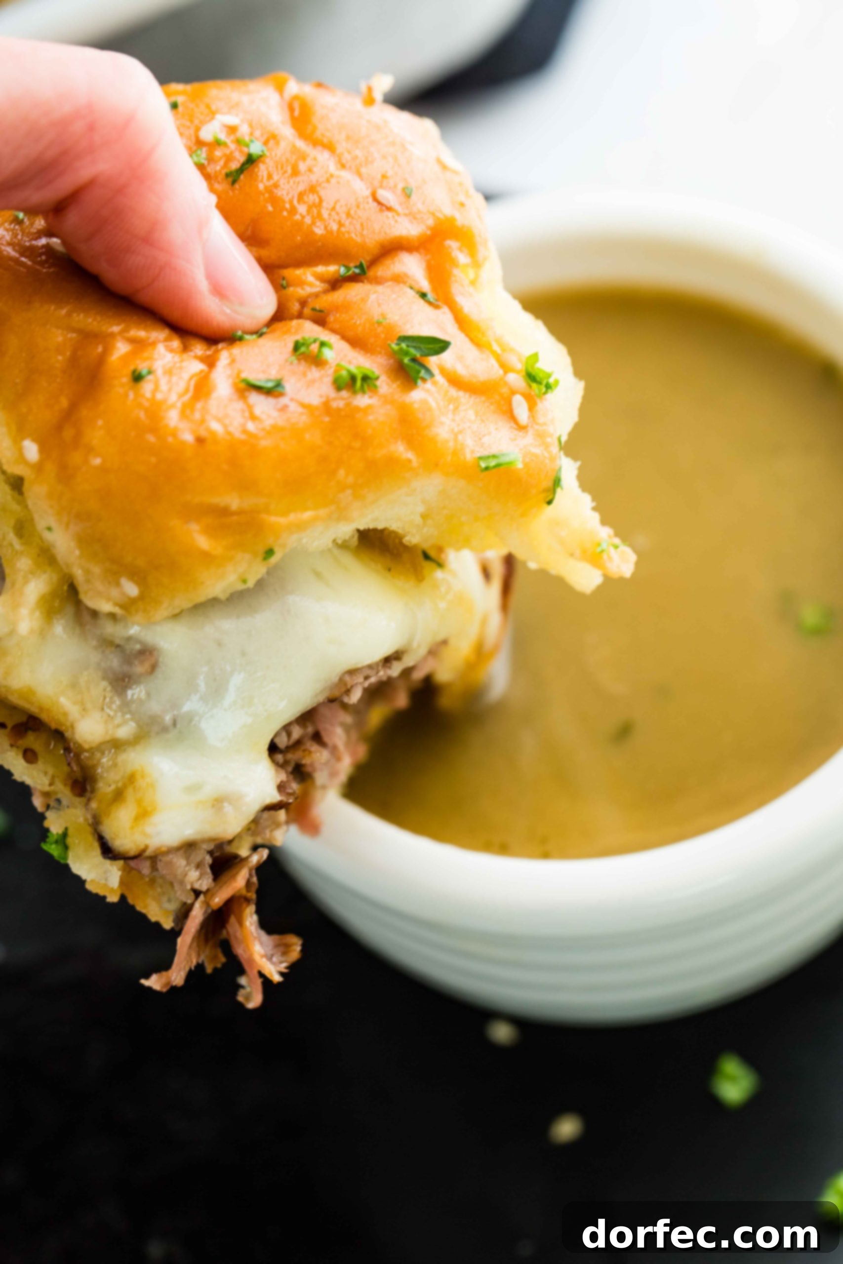 A photo of someone holding a single french dip slider about to dip it into a cup of aus jus.