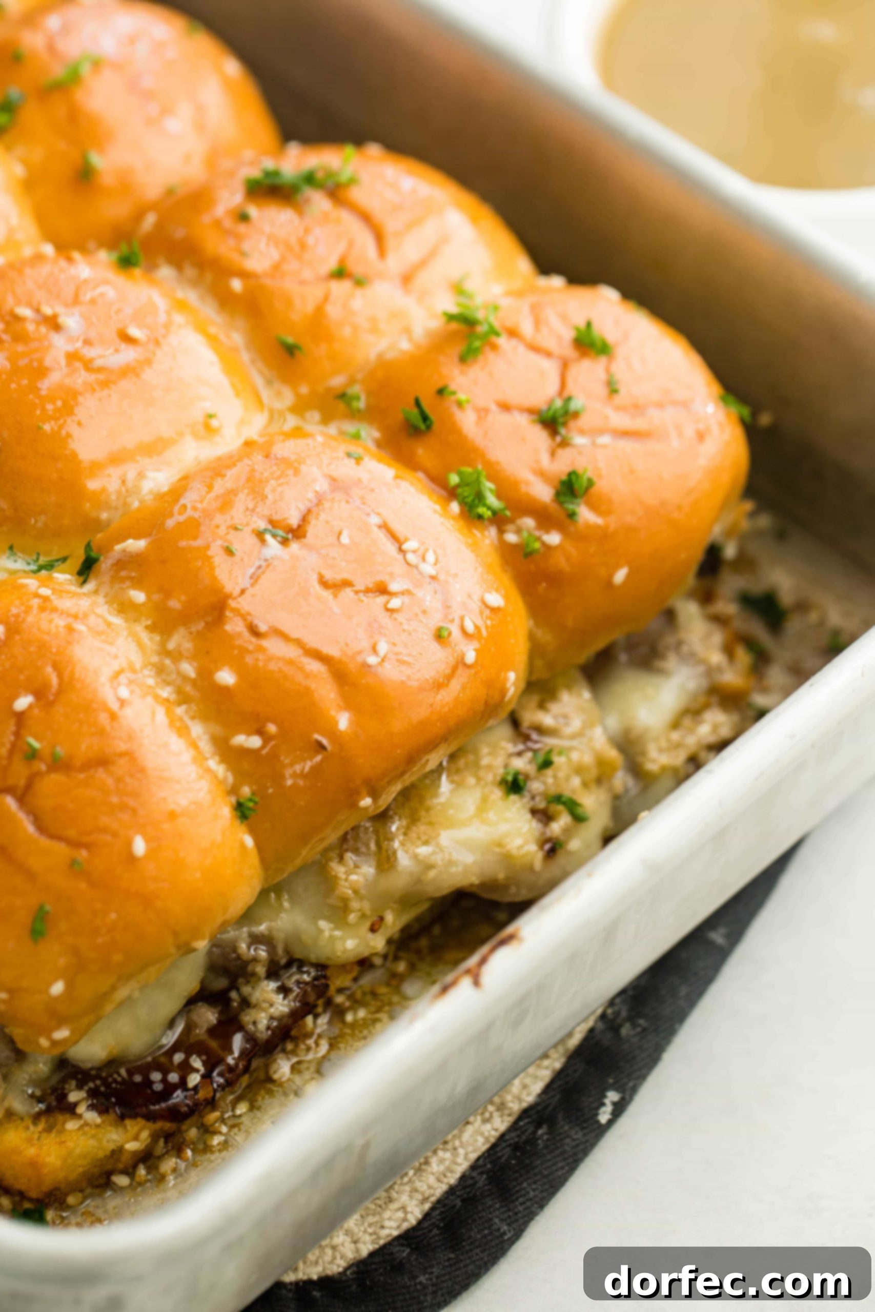 A photo of a pan full of perfectly baked french dip sliders, golden brown and cheesy.