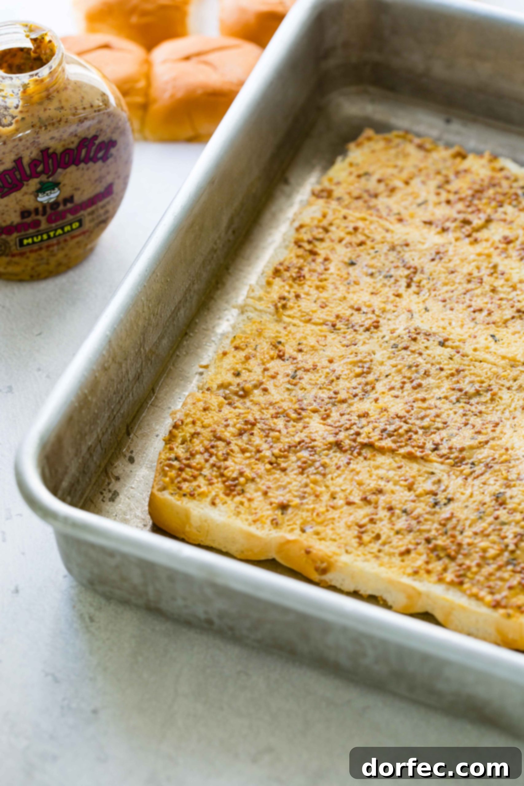 A photo of french dip slider being assembled with the mustard added to the rolls, spread evenly.