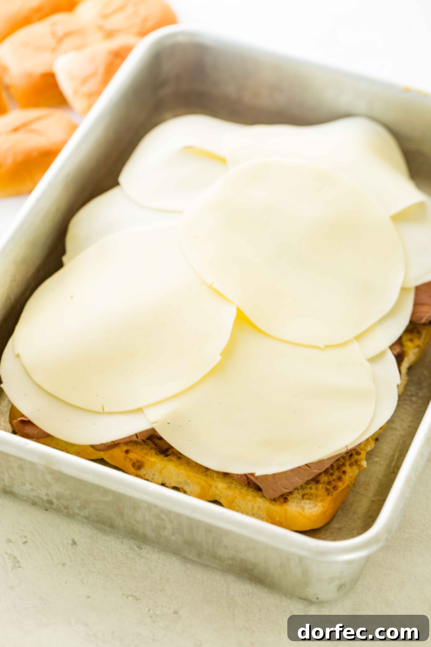 A photo of french dip sliders being constructed with a layer of provolone added on top of the roast beef.