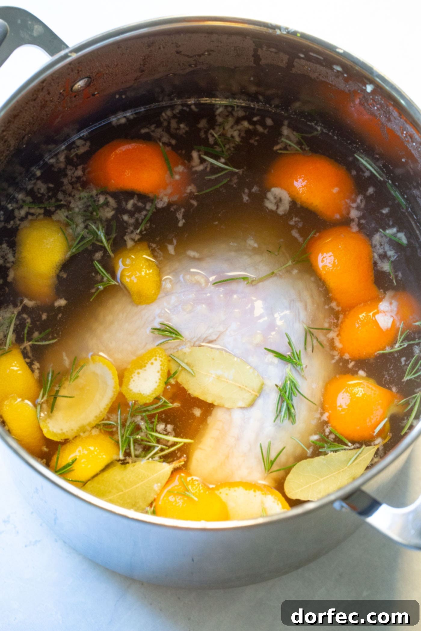 A photo of a whole turkey submerged in a flavorful brine solution within a large stock pot, illustrating the brining process.