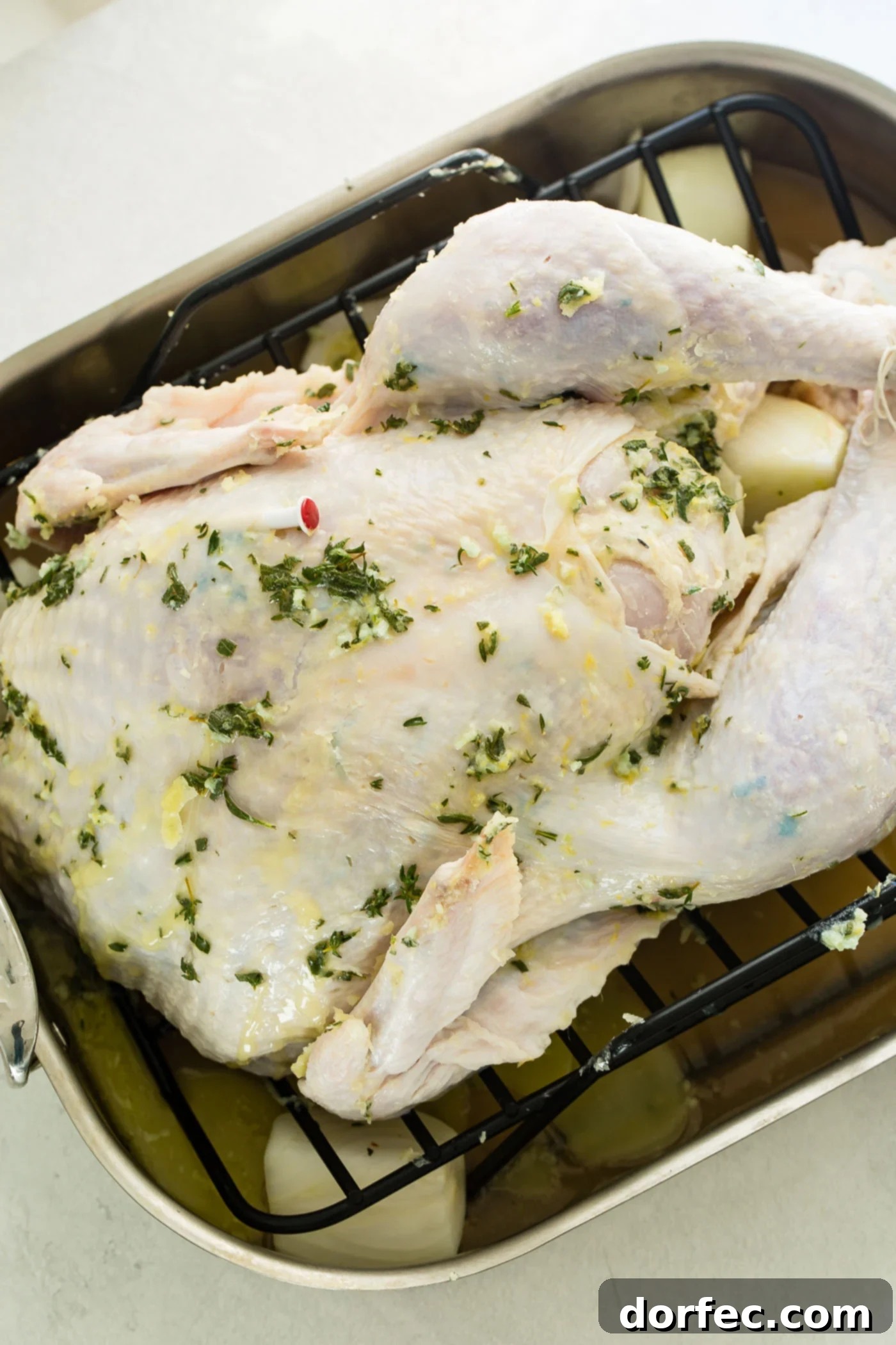 A photo of an uncooked whole turkey generously lathered in herb butter, resting in a roasting pan, ready for the oven.