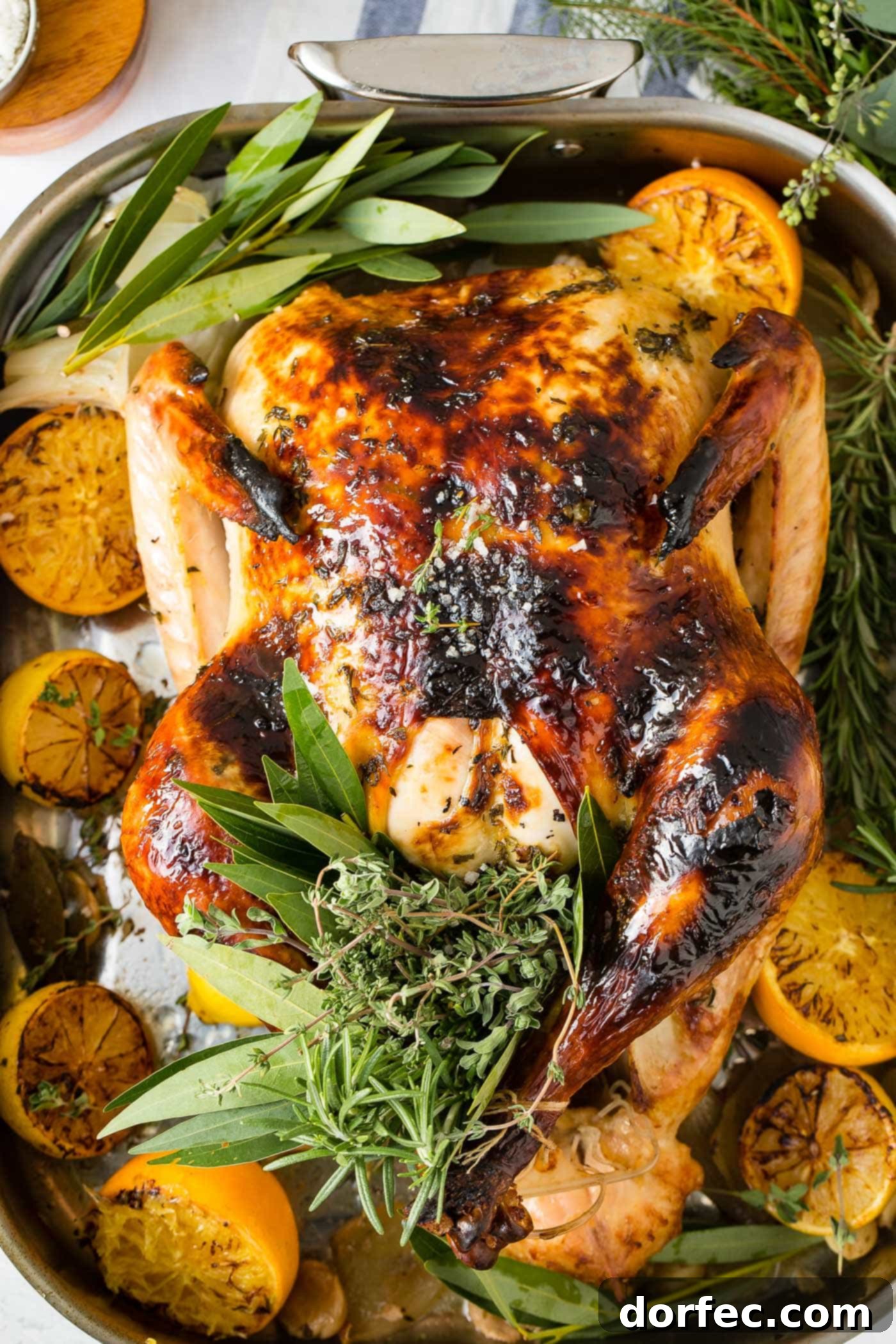 A photo of a whole roasted turkey on a platter surrounded by roasted lemon halves and bunches of fresh herbs, ready to be served.