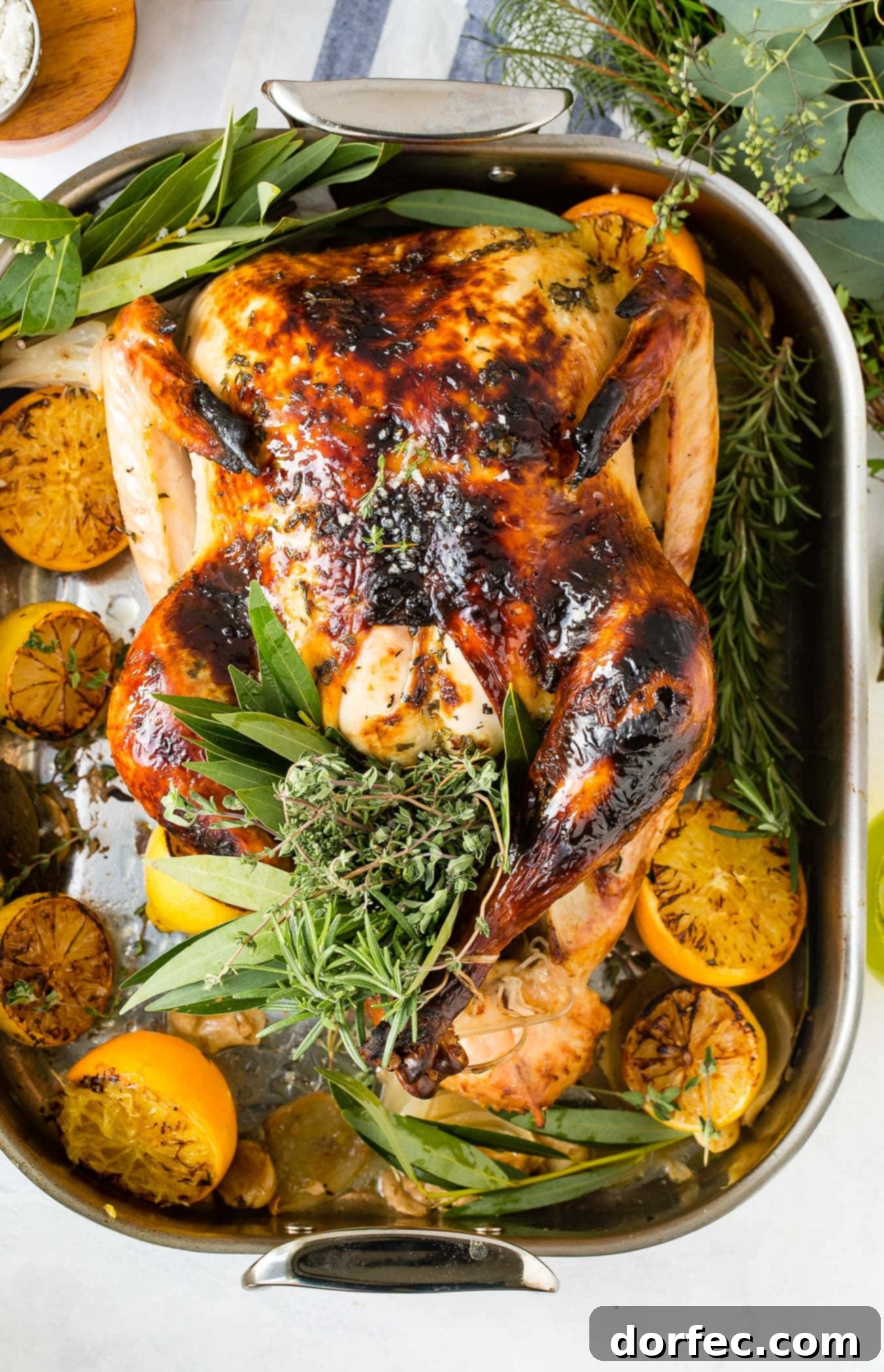 A photo of a whole roasted turkey on a platter surrounded by roasted lemon halves and bunches of fresh herbs, emphasizing its golden and succulent appearance.