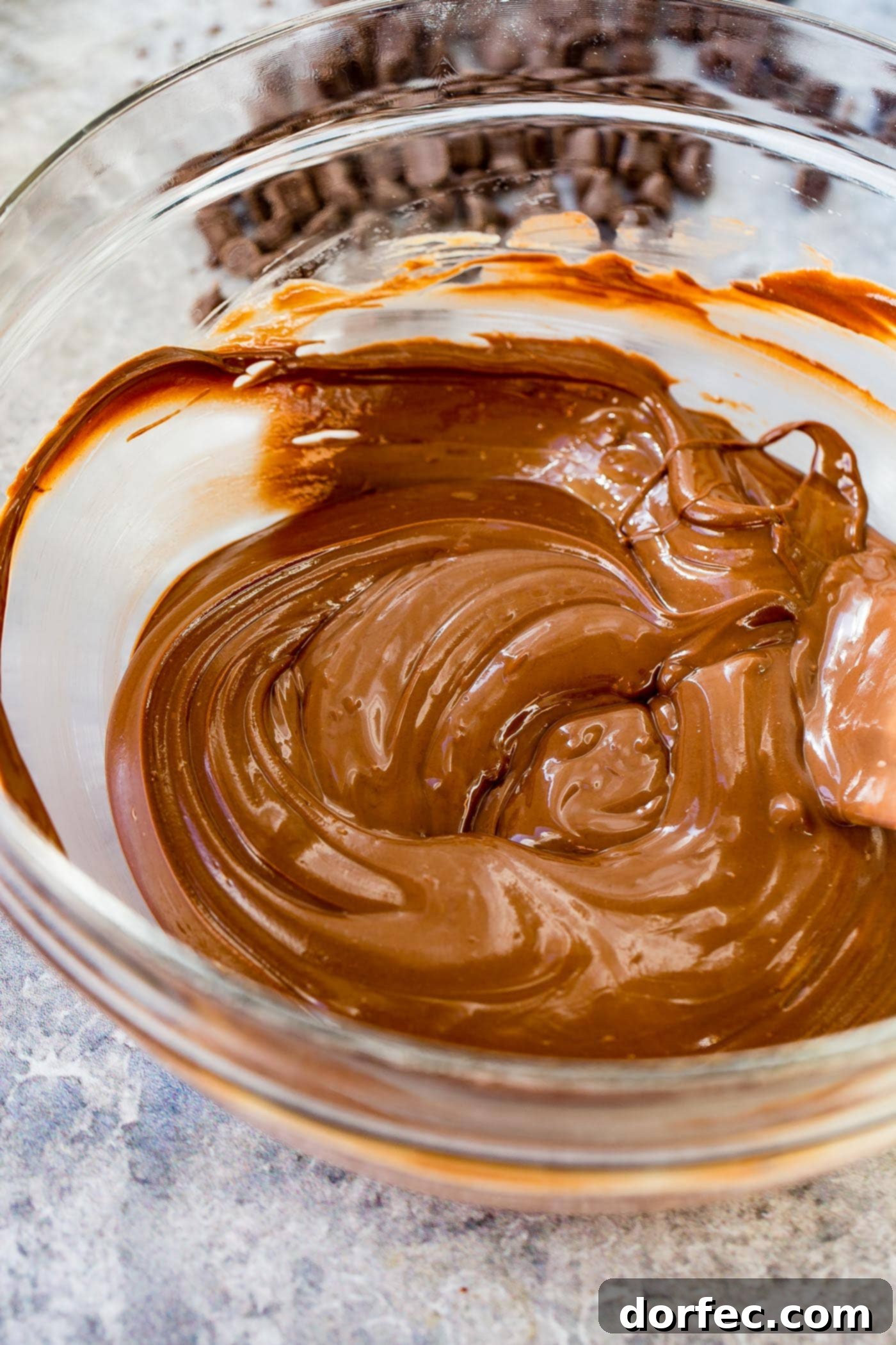 A glass bowl full of melted chocolate chips, peanut butter and butter being stirred together.