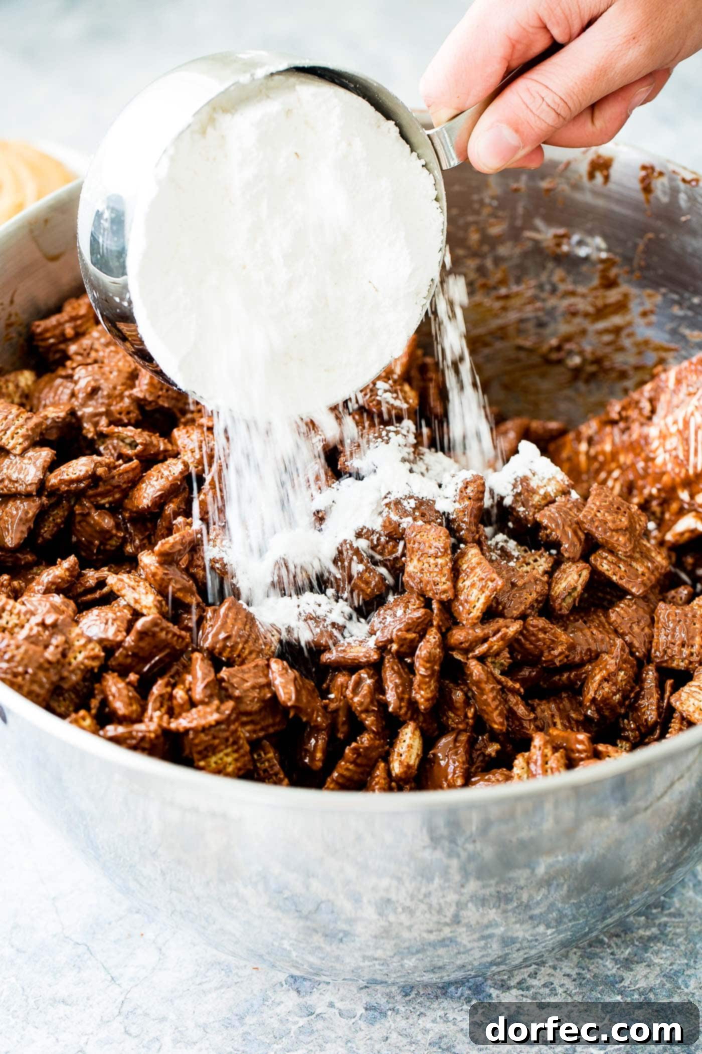 A photo of powdered sugar being add to Chex cereal that has been coated with melted chocolate and peanut butter.