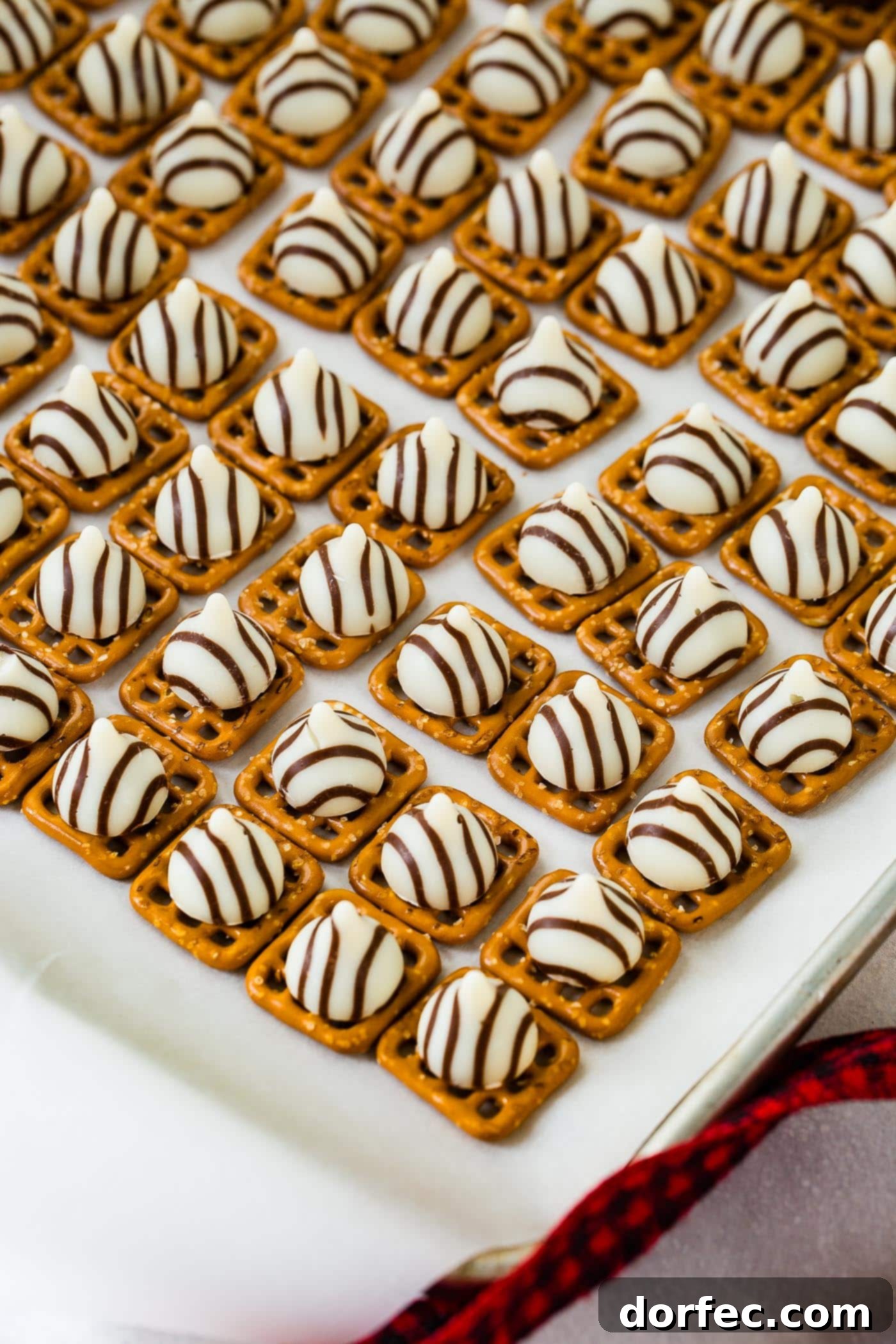 a cookie sheet lined with square pretzels and topped with Hershey's hugs