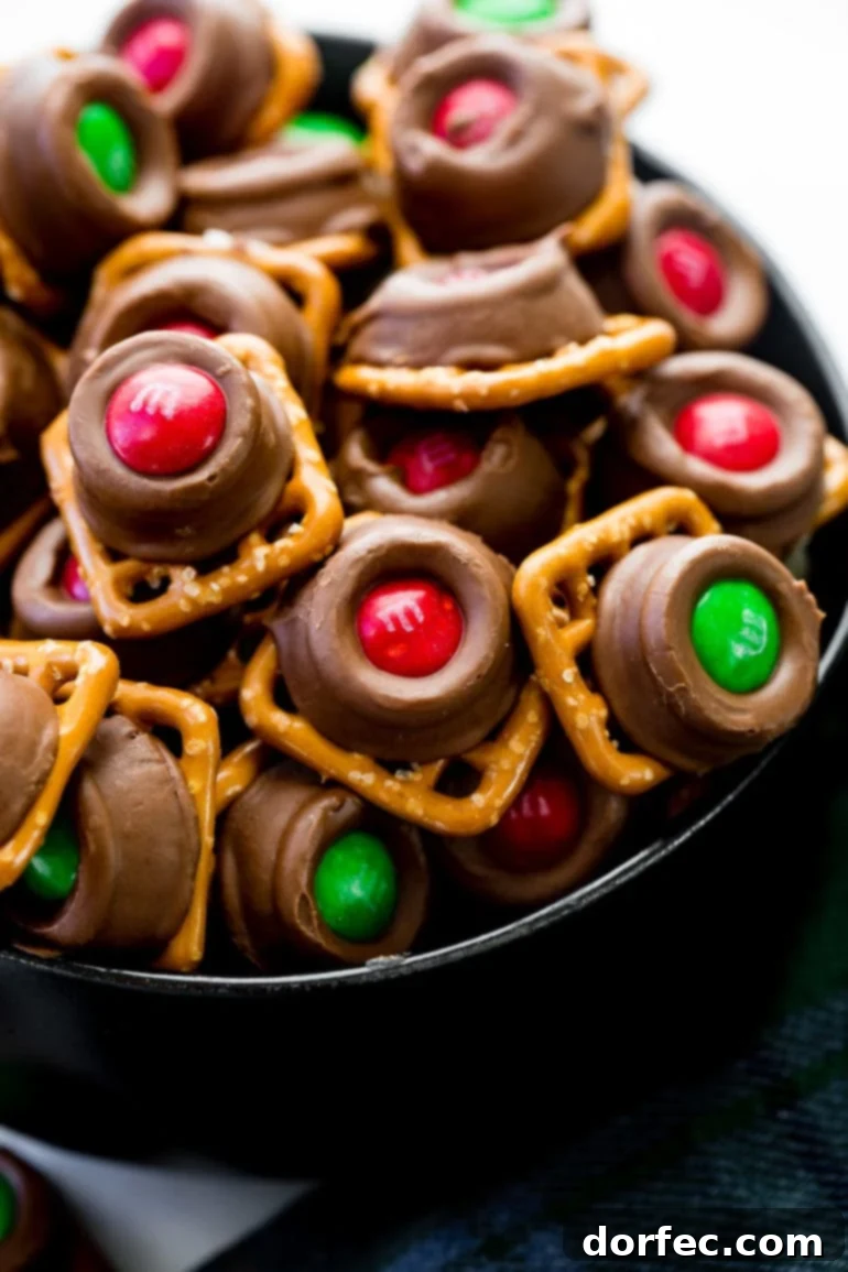A vibrant pile of Rolo Pretzel Bites, each featuring a crisp square pretzel topped with a melted Rolo caramel chocolate and a colorful Christmas M&M.