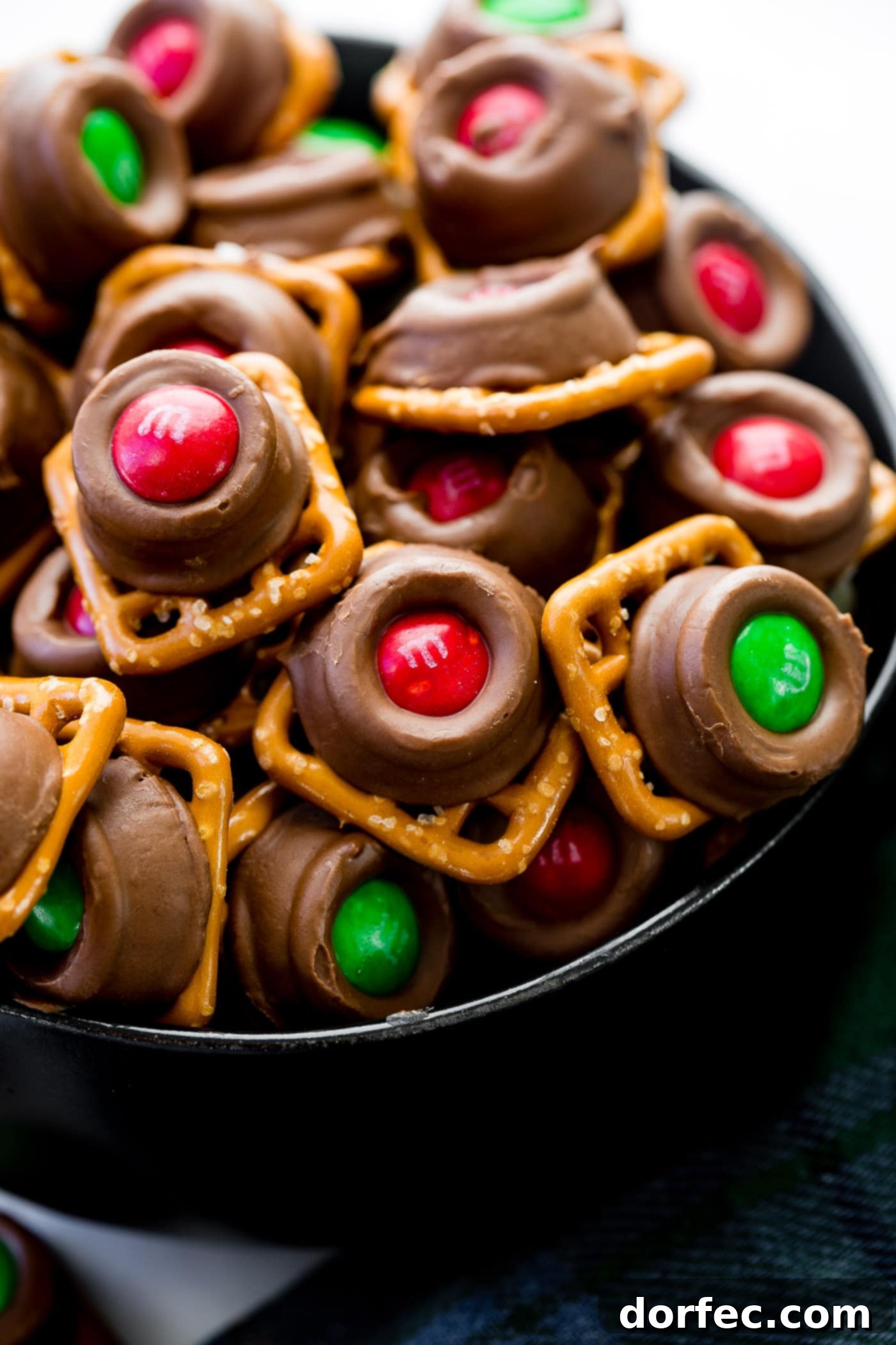 A stack of square pretzels crowned with gooey Rolos—milk chocolates filled with rich caramel—and adorned with vibrant Christmas M&Ms. These Rolo Pretzel Bites with M&Ms are a truly festive and perfect holiday treat!