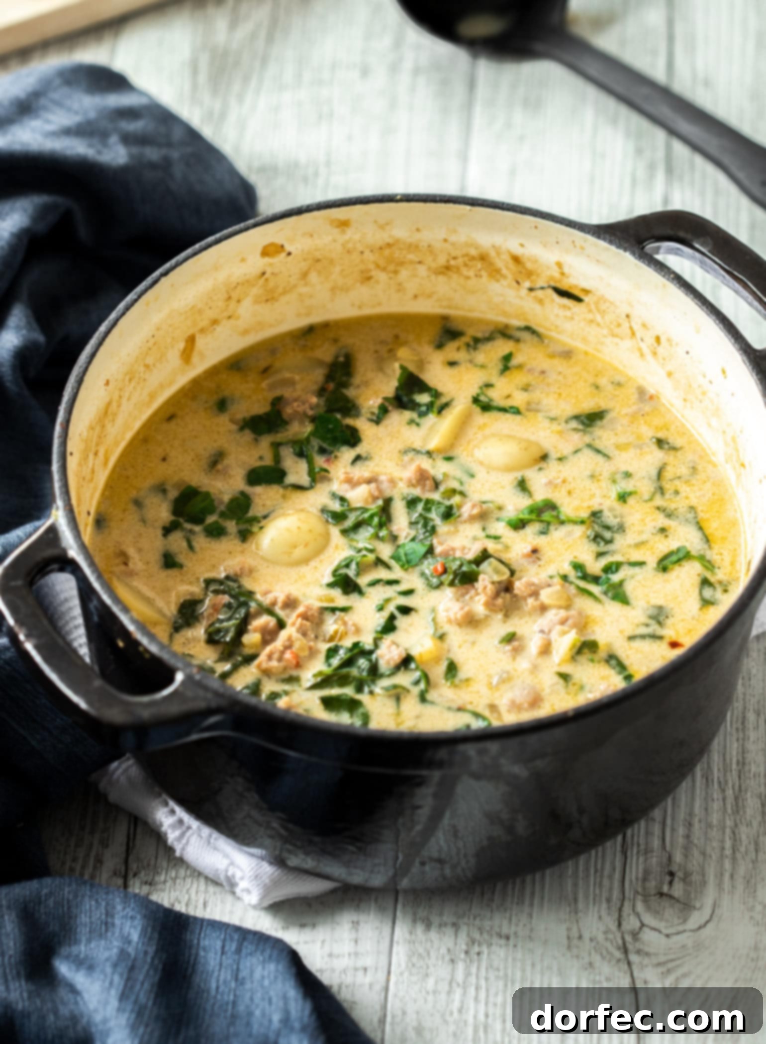 A pot of creamy zuppa toscana soup on a white timber table.