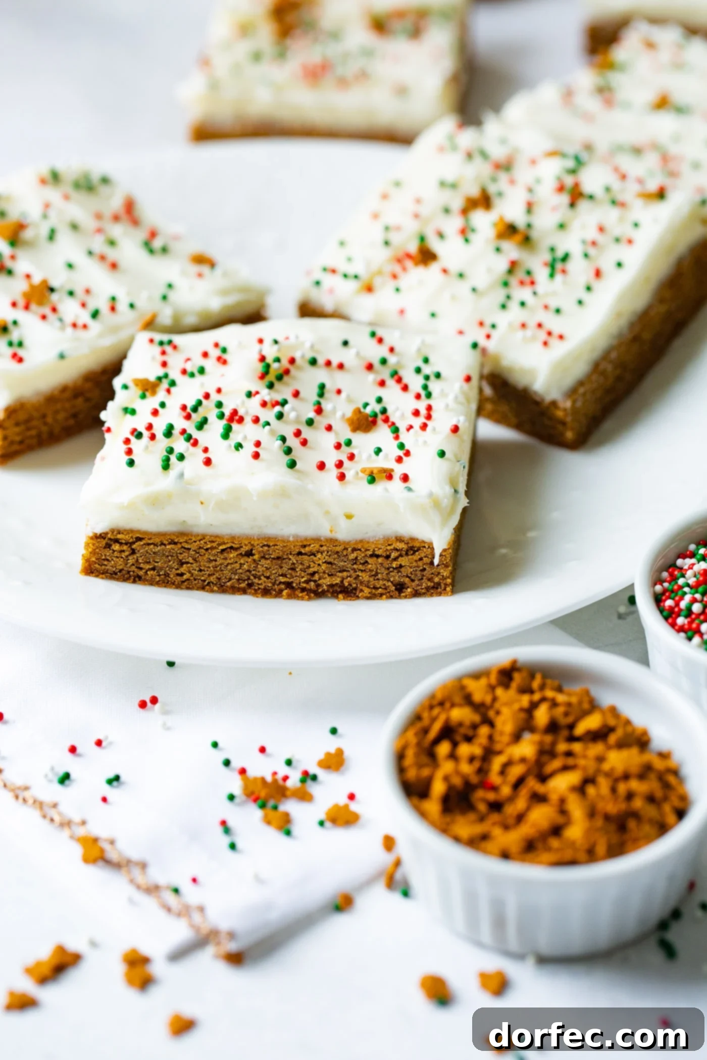 A photo of gingerbread bas sitting on a white plate with cream cheese frosting and holiday sprinkles.