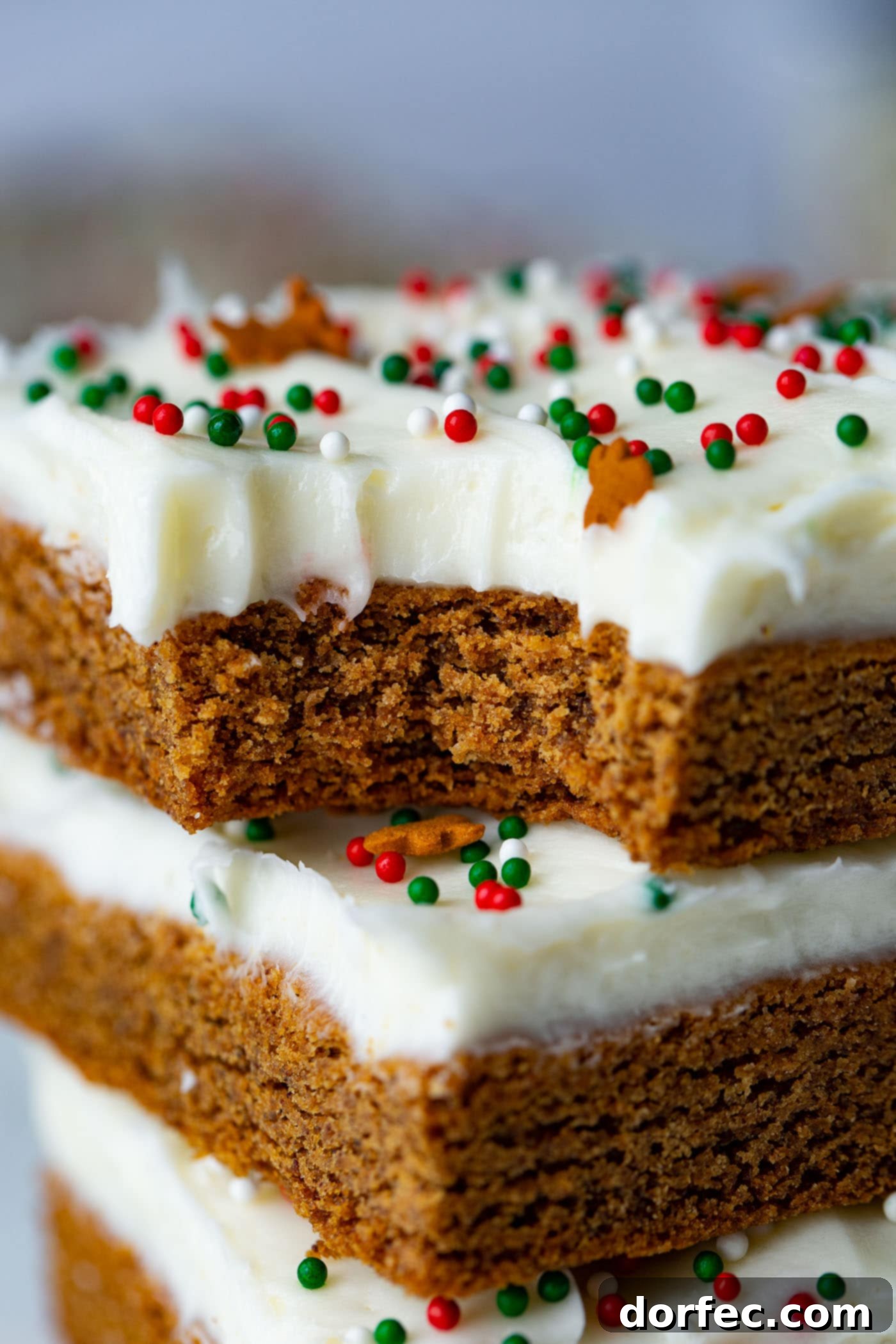 A stack of gingerbread bars frosted with cream cheese frosting and bite taken out of the top bar.