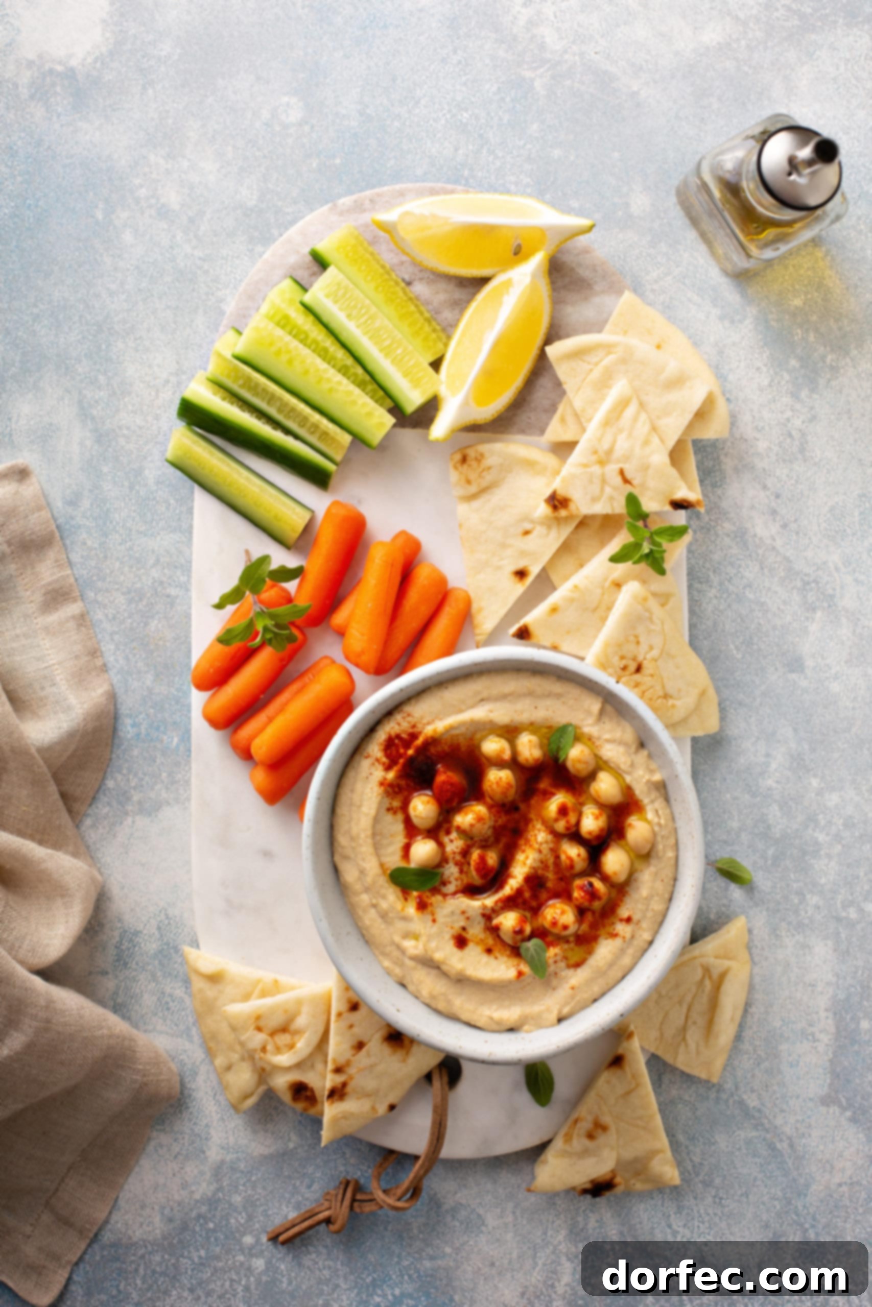 Best Easy Homemade Hummus A tray with baby carrots, celery sticks, lemon wedges and tortilla wedges sitting next to a bowl of hummus with whole chick peas on top and sprinkled with smoked paprika