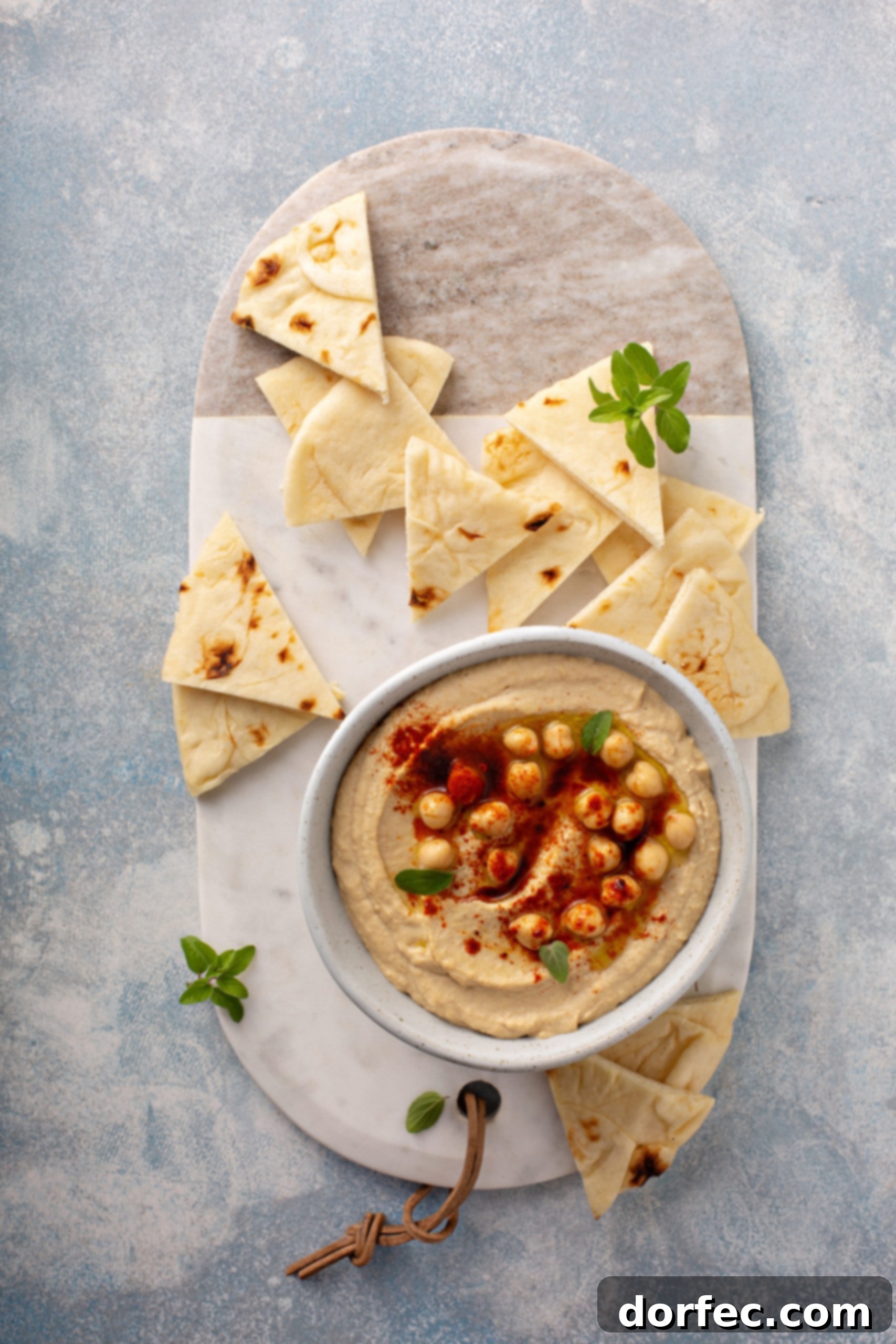 Best Easy Homemade Hummus A bowl of hummus with whole chick peas and smoked paprika sprinkled on top and tortilla wedges in the back ground.