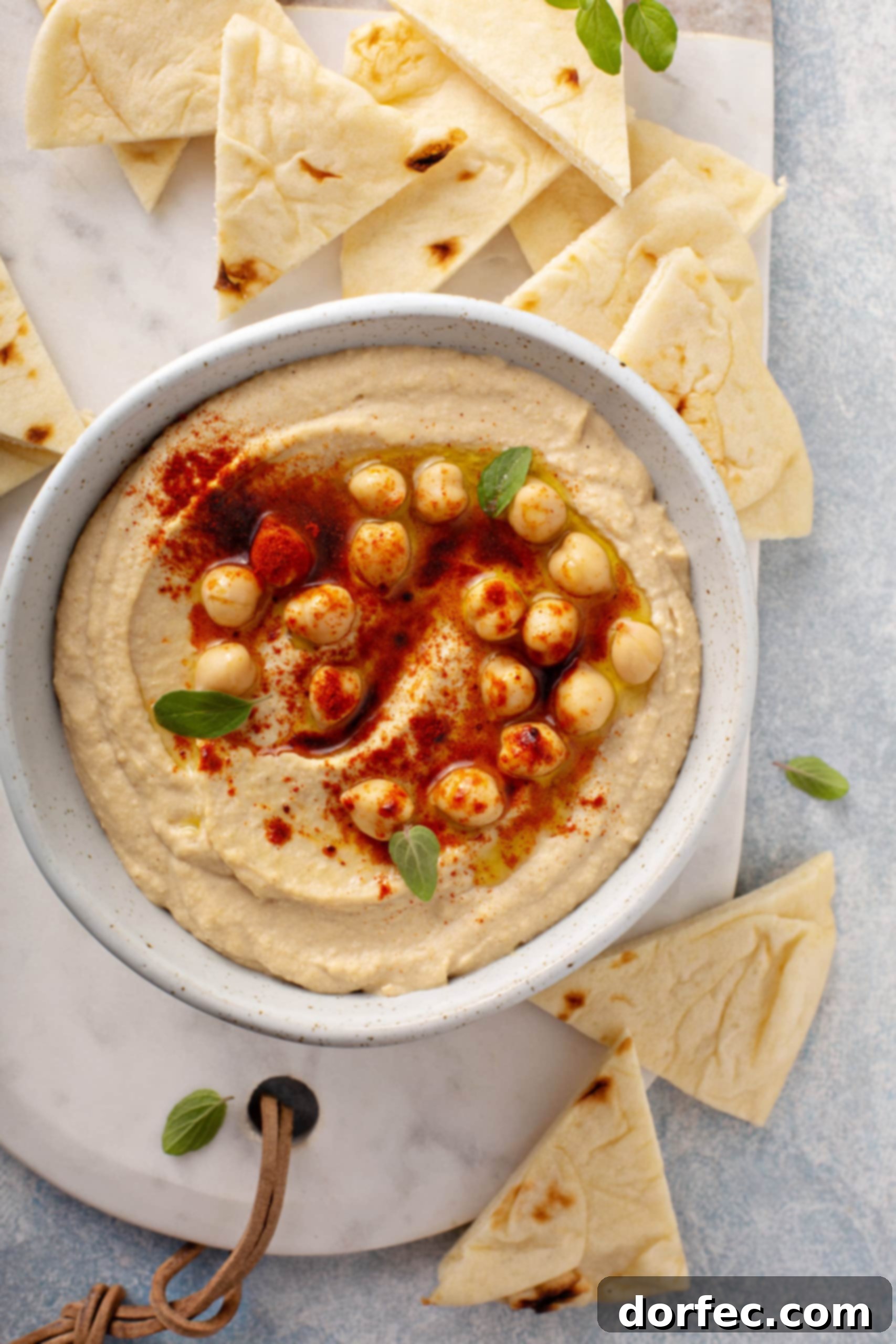 Best Easy Homemade Hummus A close-up picture of a bowl of hummus with chick peas and smoked paprika sprinkled on top, and surrounded with flour tortilla wedges.