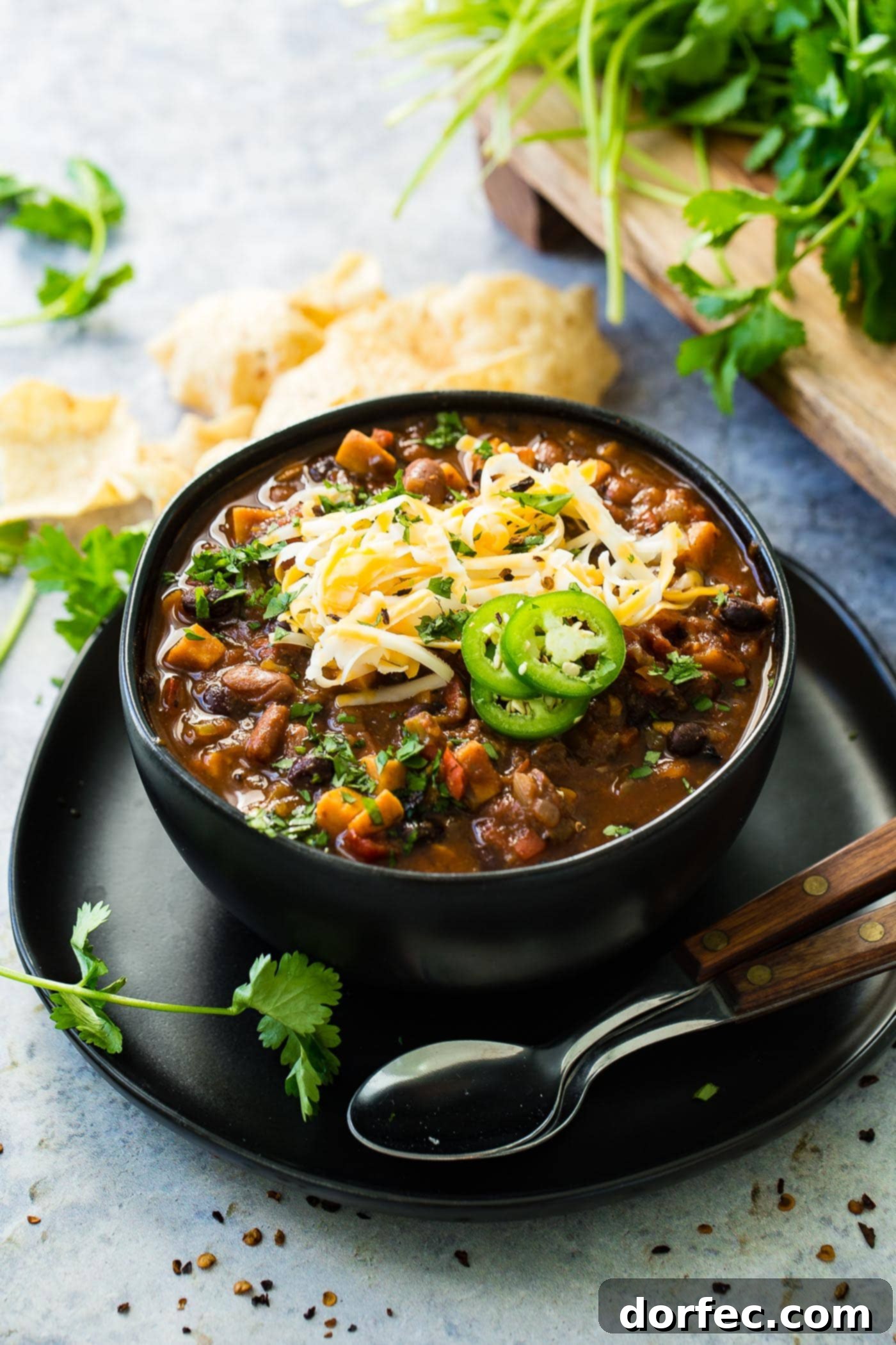 Instant Pot Vegetarian Chili A warm, inviting bowl of Instant Pot meatless chili, generously topped with a blanket of shredded cheese and bright slices of fresh jalapeño, with two spoons poised for enjoyment beside it, evoking a sense of comforting warmth.