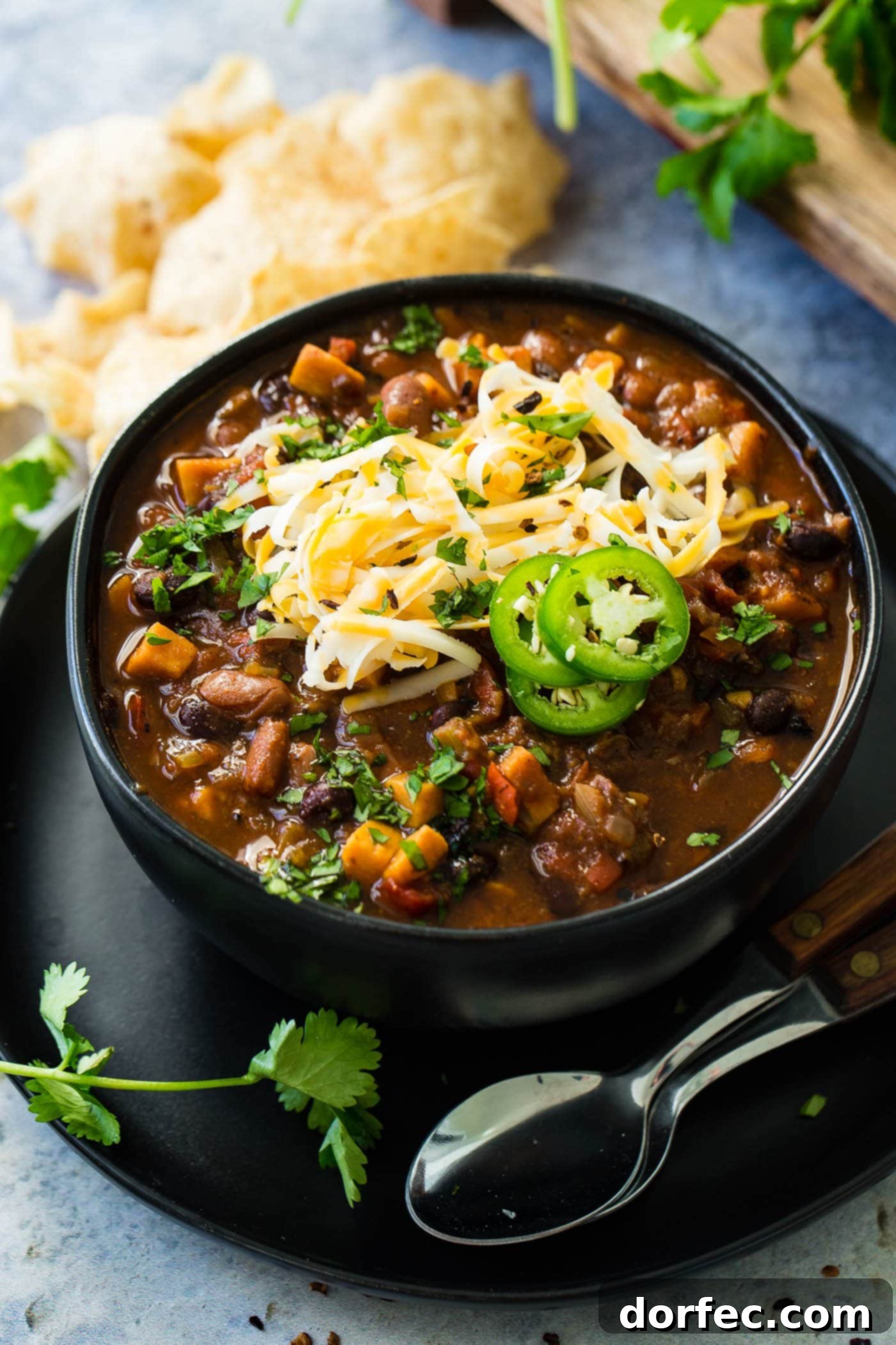 Instant Pot Vegetarian Chili A bowl of wholesome veggie chili, generously adorned with shredded cheese and vibrant jalapeño slices, with two spoons invitingly placed beside it, signifying a comforting and ready-to-eat meal.