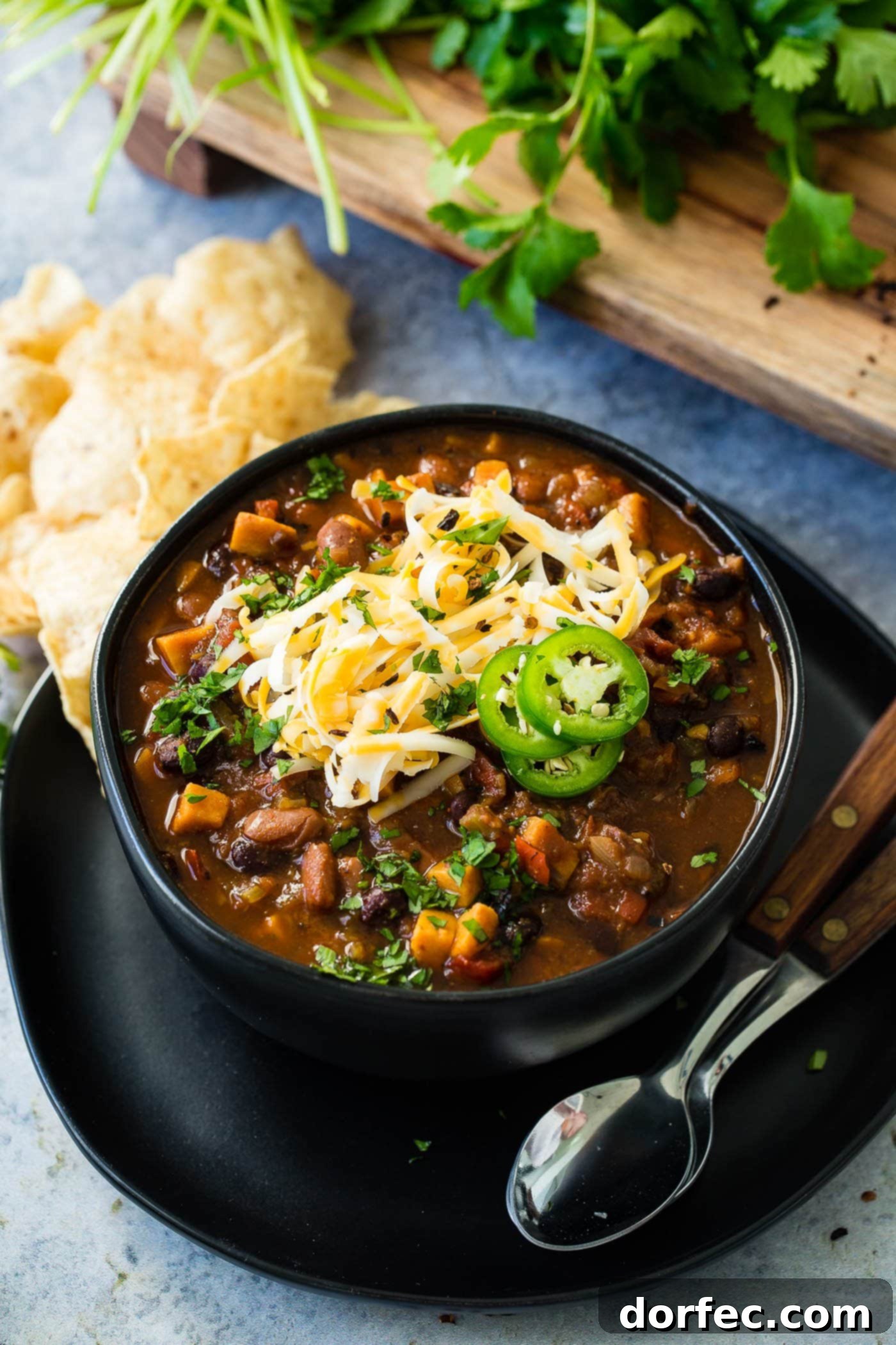 Instant Pot Vegetarian Chili A cozy bowl of Instant Pot meatless chili, generously adorned with shredded cheese and vibrant jalapeño slices, with two spoons patiently waiting beside it for a comforting meal.