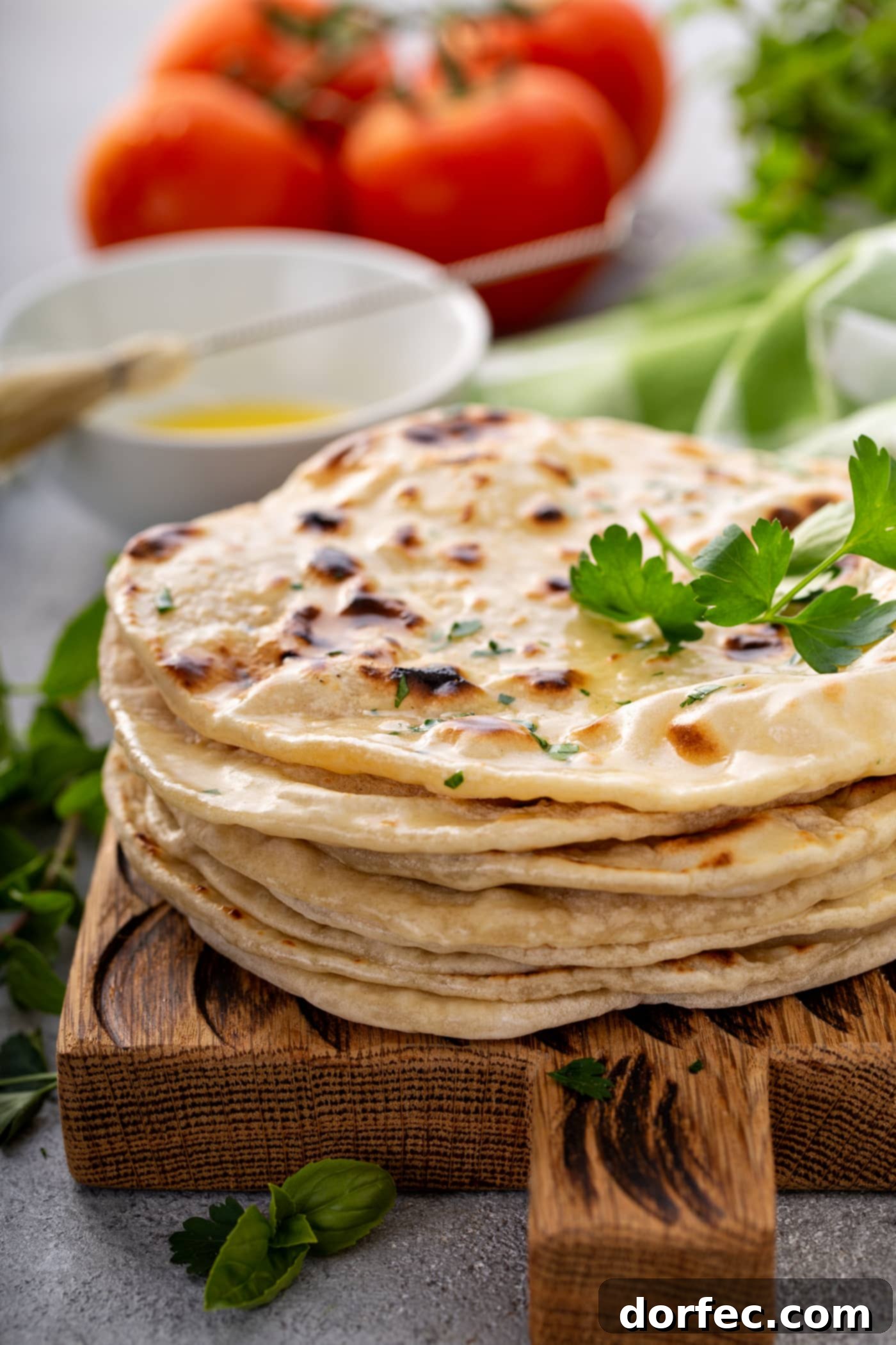 A stack of freshly cooked bread discs, generously topped with vibrant chopped fresh parsley and a sprig of parsley for garnish.