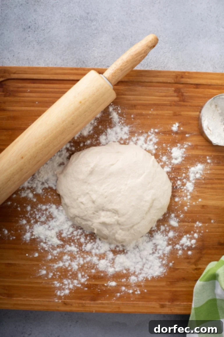 A mound of unleavened bread dough resting on a floured wooden cutting board with a rolling pin beside it.
