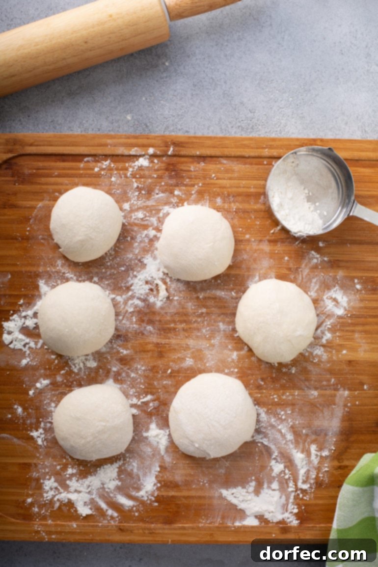 Six evenly portioned balls of unleavened bread dough on a floured wooden cutting board, ready for rolling.