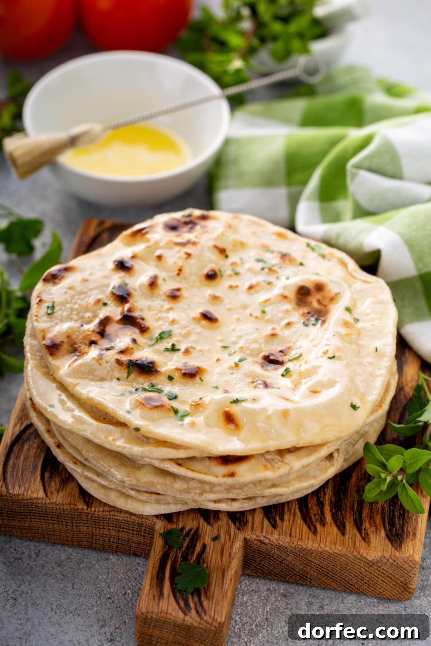 A stack of freshly cooked unleavened bread discs, topped with chopped fresh herbs.