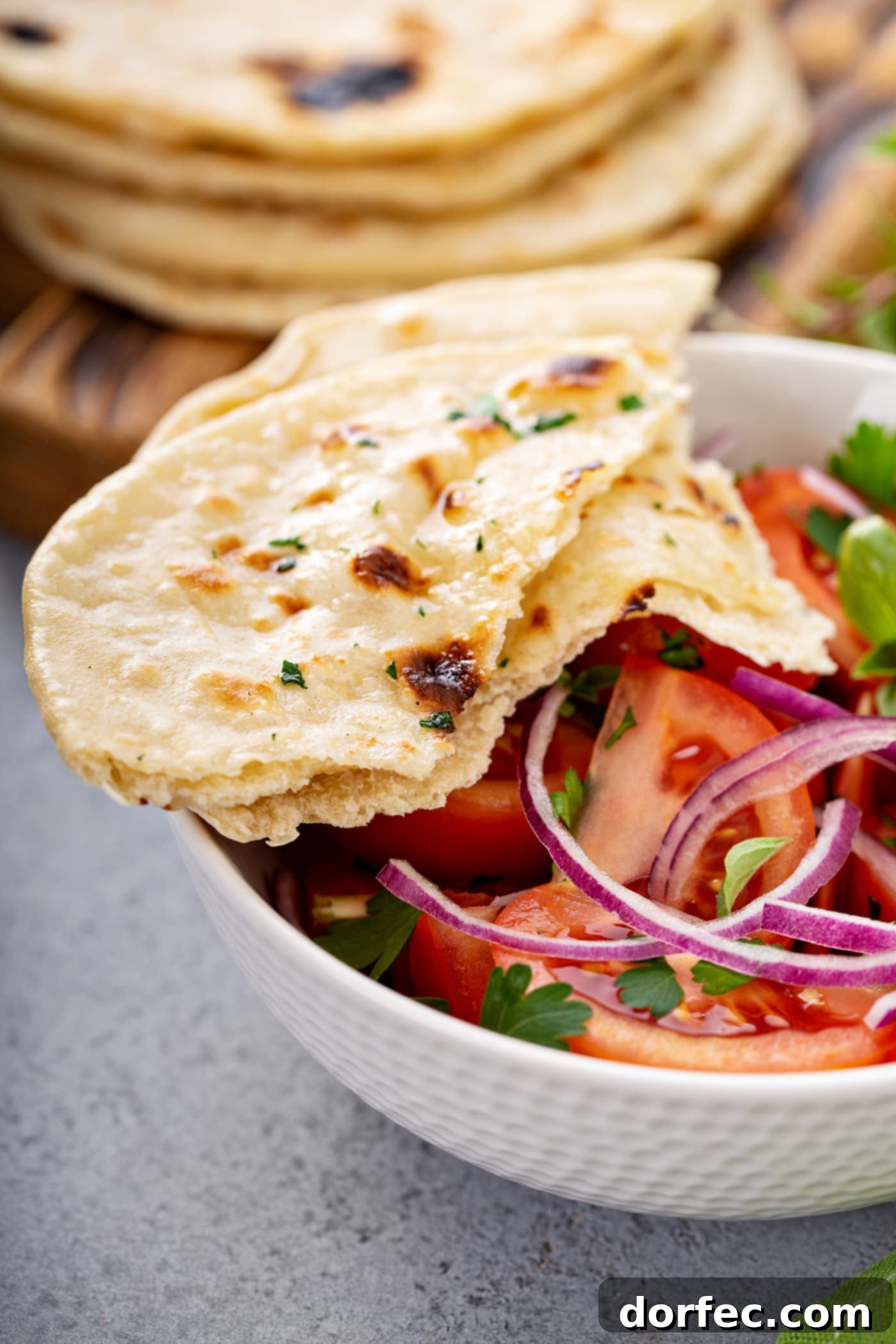 A vibrant bowl of fresh tomato and onion salad, served with pieces of golden unleavened flatbread on the side.