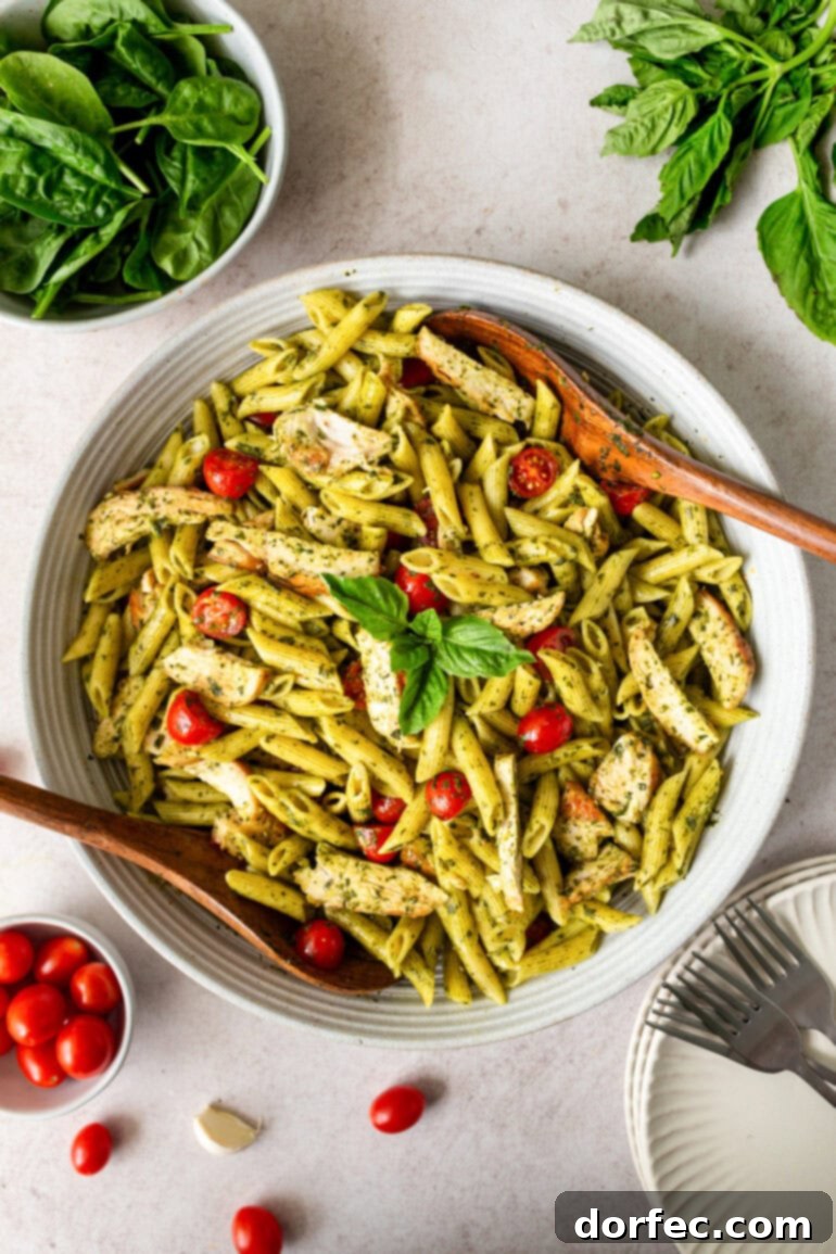 Zesty Lemon Basil Chicken Pasta 8 A tantalizing photo of a large bowl of penne pasta tossed in a bright green sauce, adorned with cherry tomatoes, tender chicken strips, and wooden serving spoons nestled within the bowl.