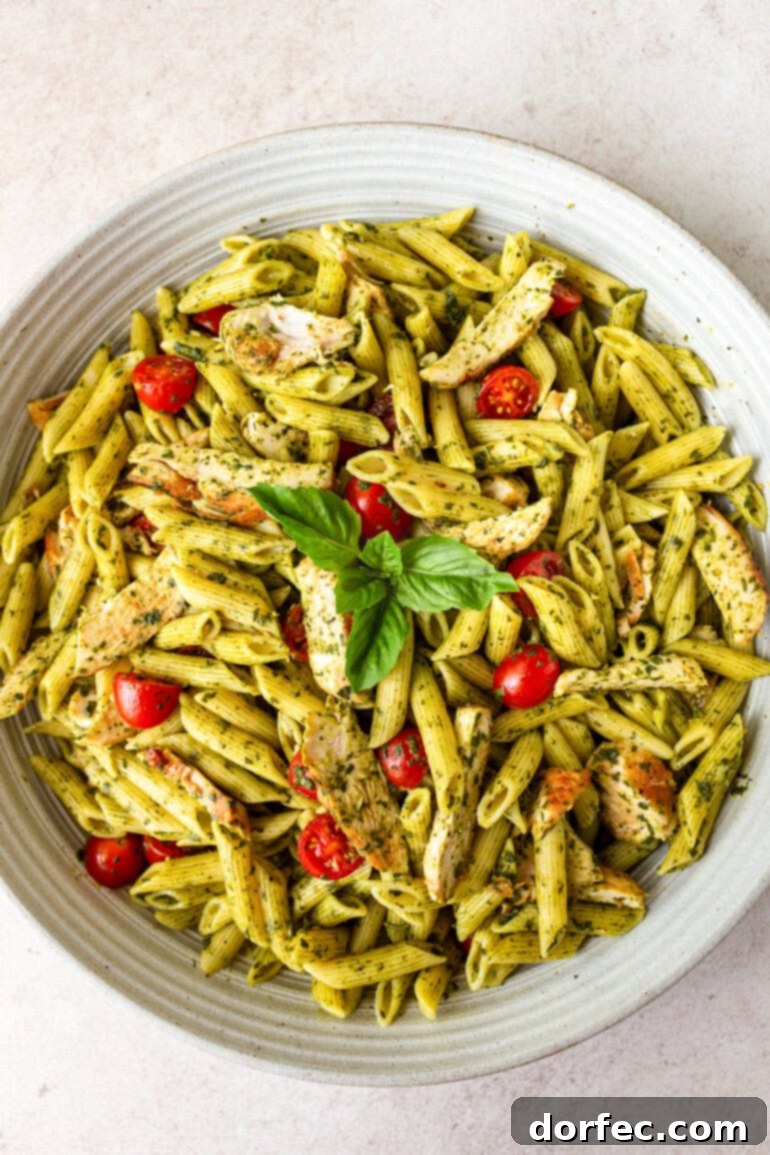 Zesty Lemon Basil Chicken Pasta 9 A photo of a large white serving bowl full of cooked penne pasta tossed with a honey lemon basil sauce, halved cherry tomatoes, and chicken strips, presented beautifully for serving.