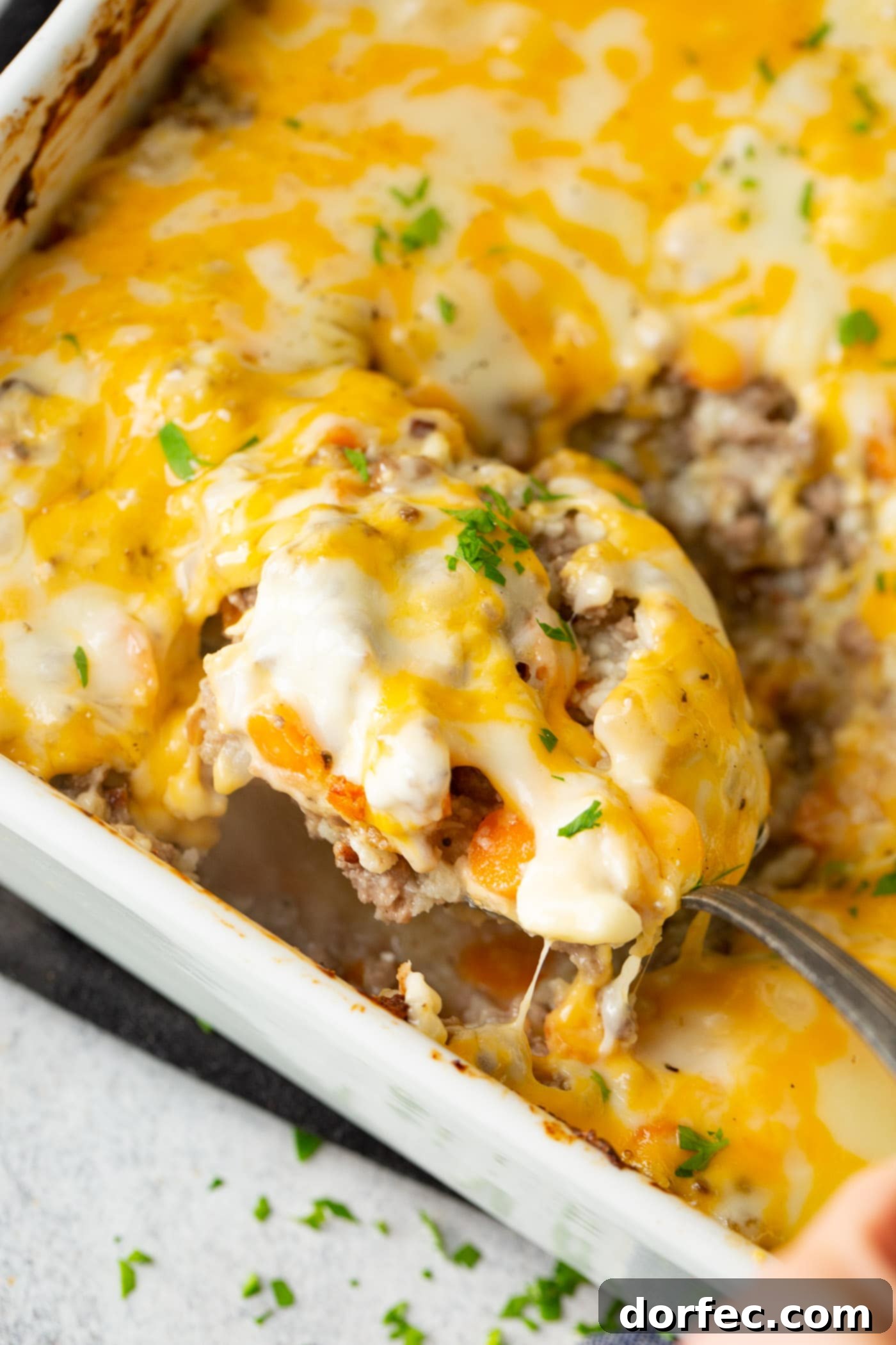 A baking dish brimming with low carb cheesy ground beef and cauliflower rice casserole, with a serving spoon poised to scoop out a generous portion, emphasizing its hearty and inviting texture.