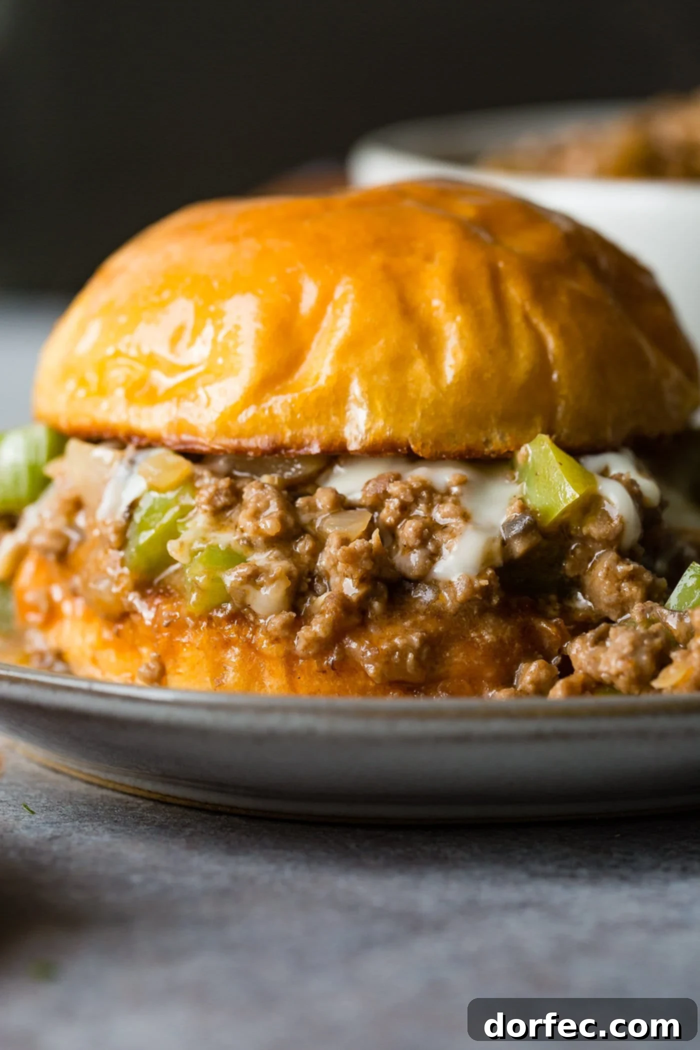 Philly Cheesesteak Sloppy Joes A photo of a philly cheesesteak sloppy joe on a toasted brioche bun on a white plate, showcasing the melted cheese and rich filling.