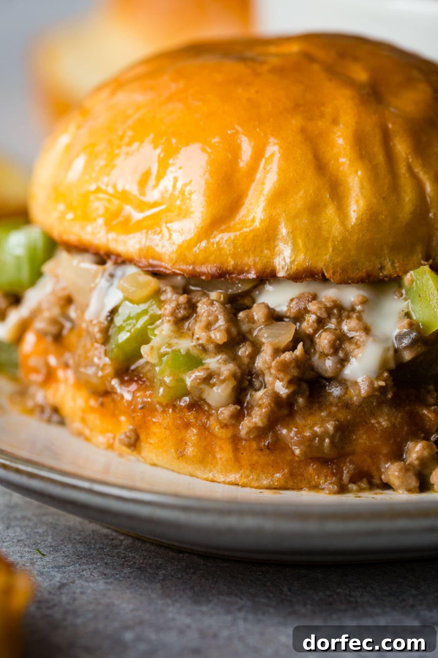 Philly Cheesesteak Sloppy Joes A closeup photo of a philly cheesesteak sloppy joe on a toasted brioche bun, with rich meat and melted cheese spilling slightly from the sides.
