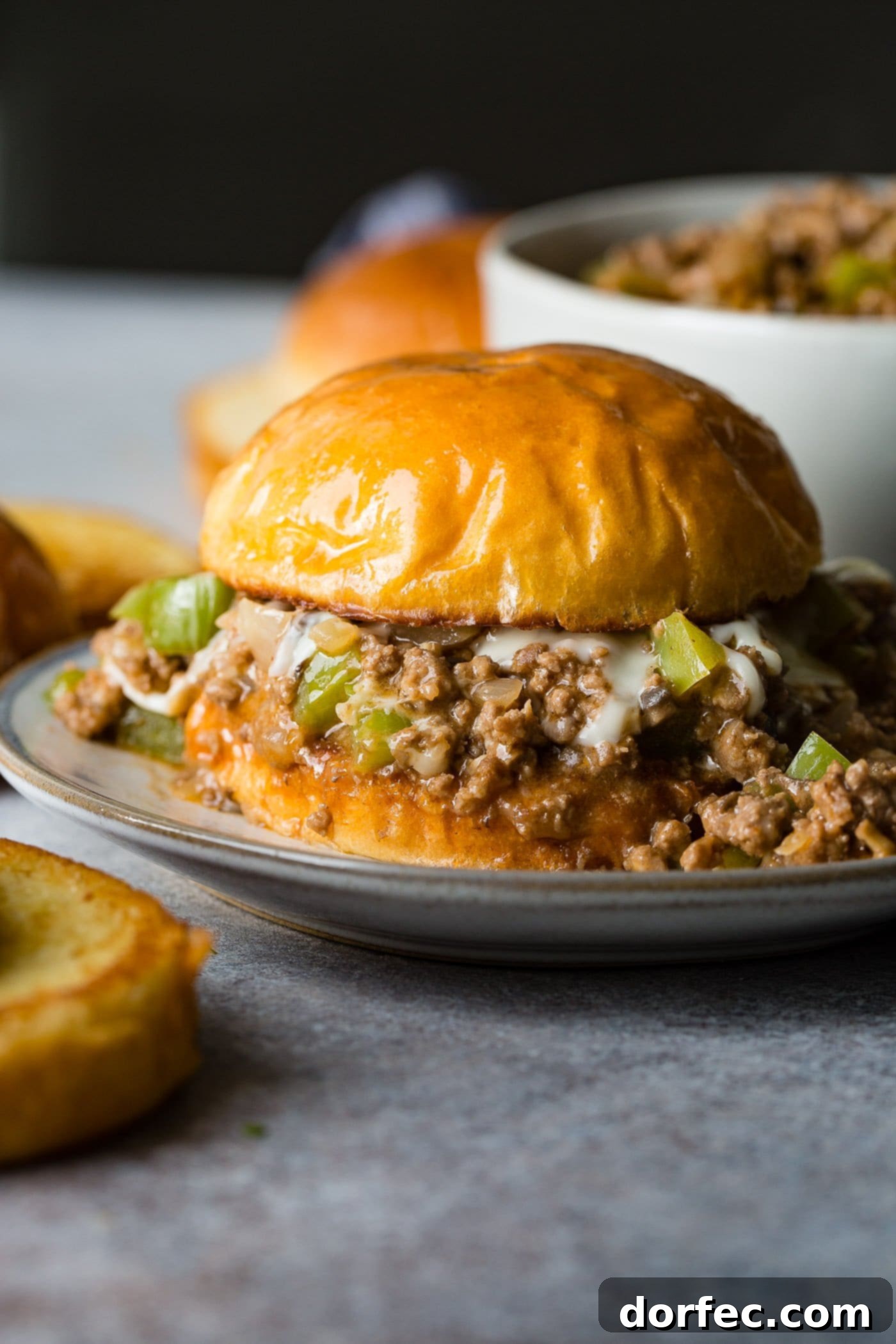 Philly Cheesesteak Sloppy Joes A photo of a philly cheesesteak sloppy joe on a toasted brioche bun on a white plate, ready to be enjoyed as part of a delicious meal.