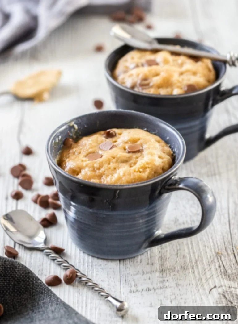 Two blue mugs filled with cake and surrounded by choco chips and spoons