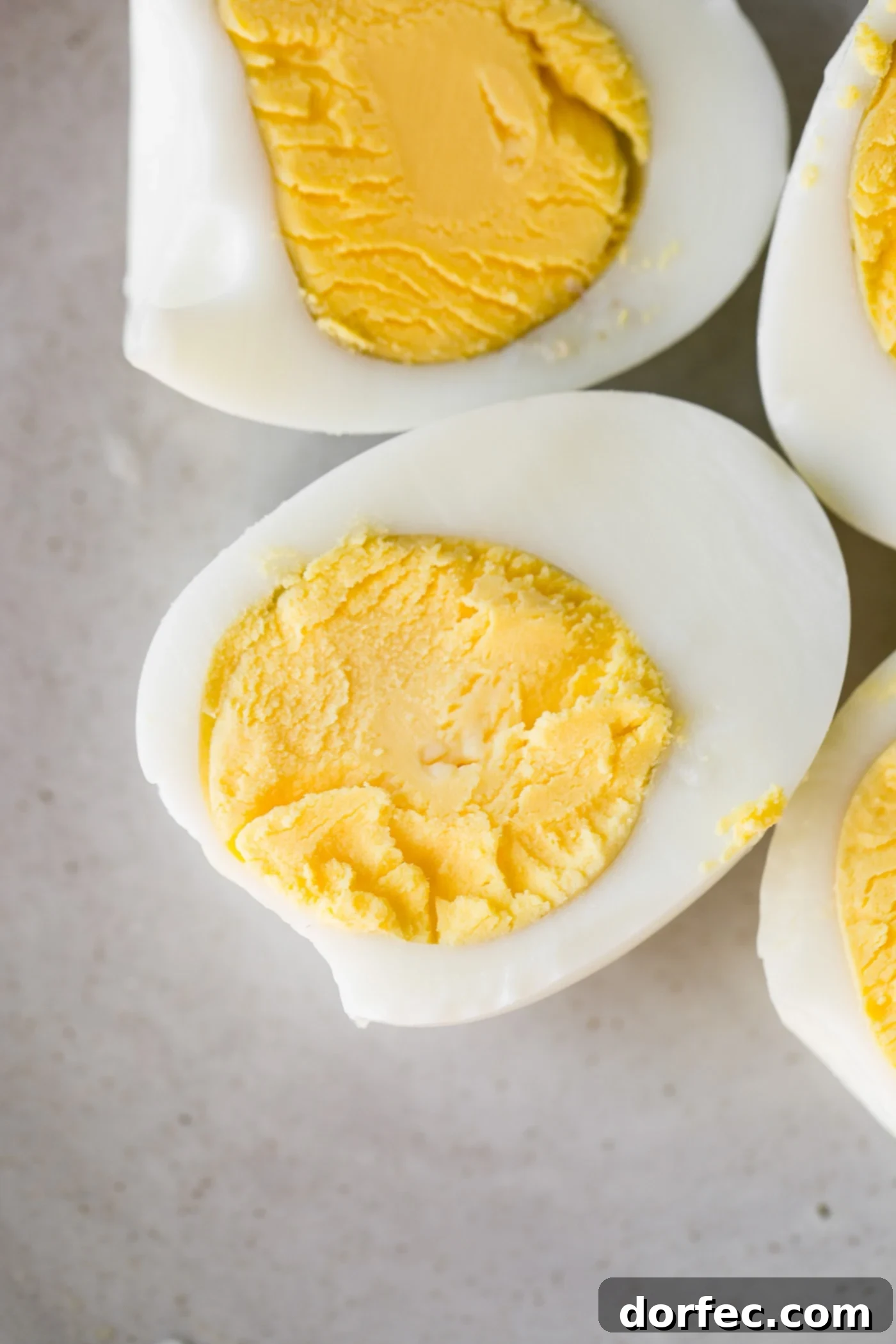 How to Make Perfect Hard Boiled Eggs Two perfectly cooked hard boiled eggs, sliced in half to reveal their vibrant yellow yolks.