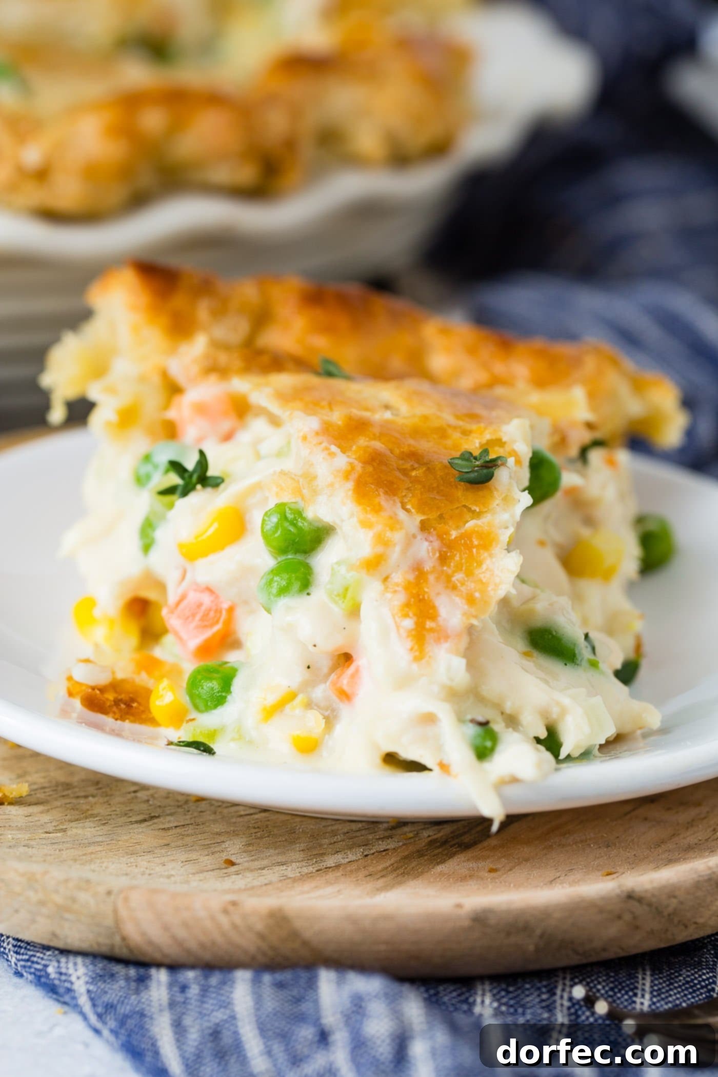 Perfectly Baked Chicken Pot Pie Slice A close-up of a generous slice of homemade chicken pot pie, showcasing its golden, flaky top crust and the abundant, creamy filling within. Visible ingredients include tender chicken pieces, bright carrots, and green peas, all bathed in a rich, savory sauce. The perfect portion for a comforting meal.